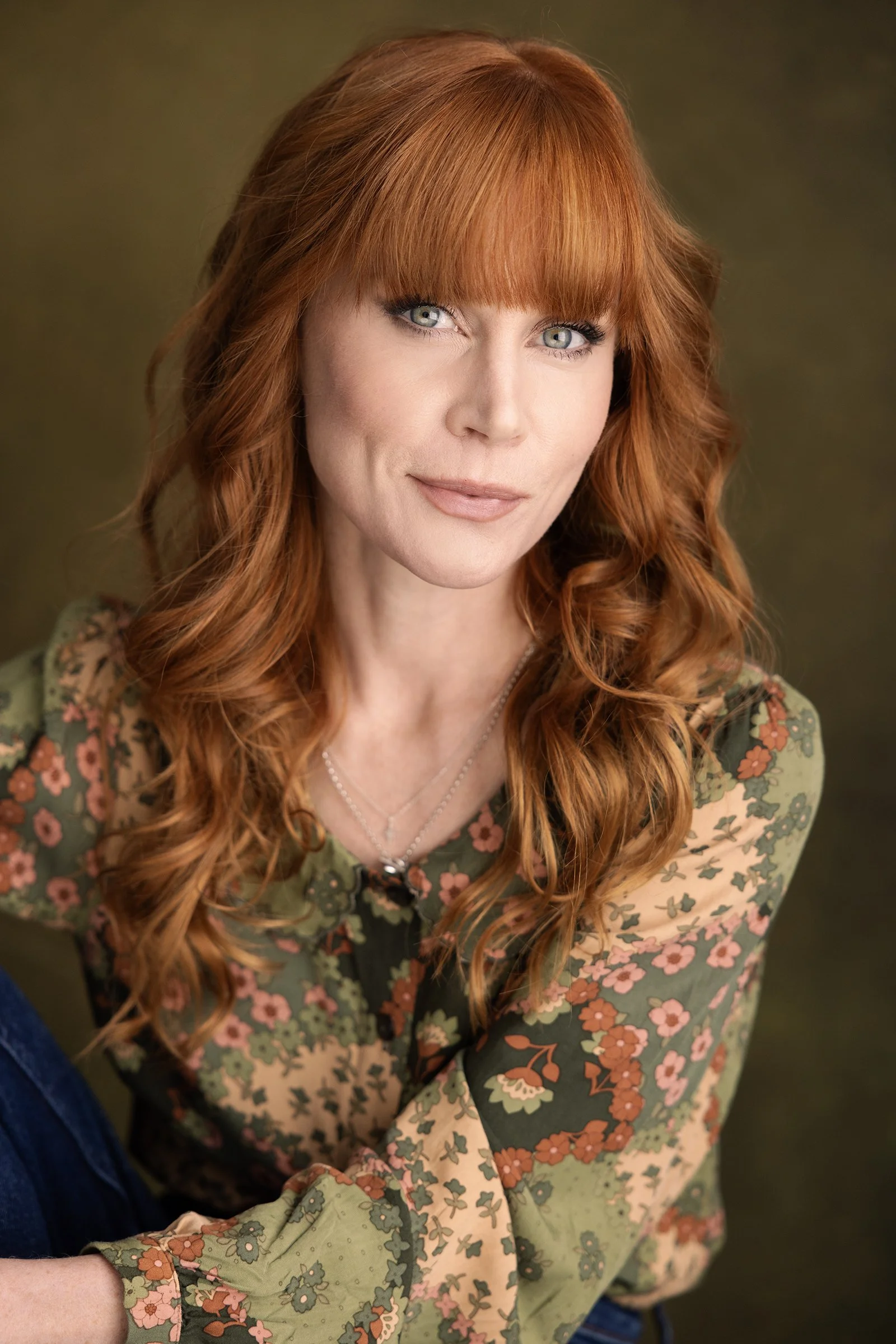 Photo of Michelle Blundell taken by Andi Crown Photography. Michelle has styled red hair and a floral long-sleeved top