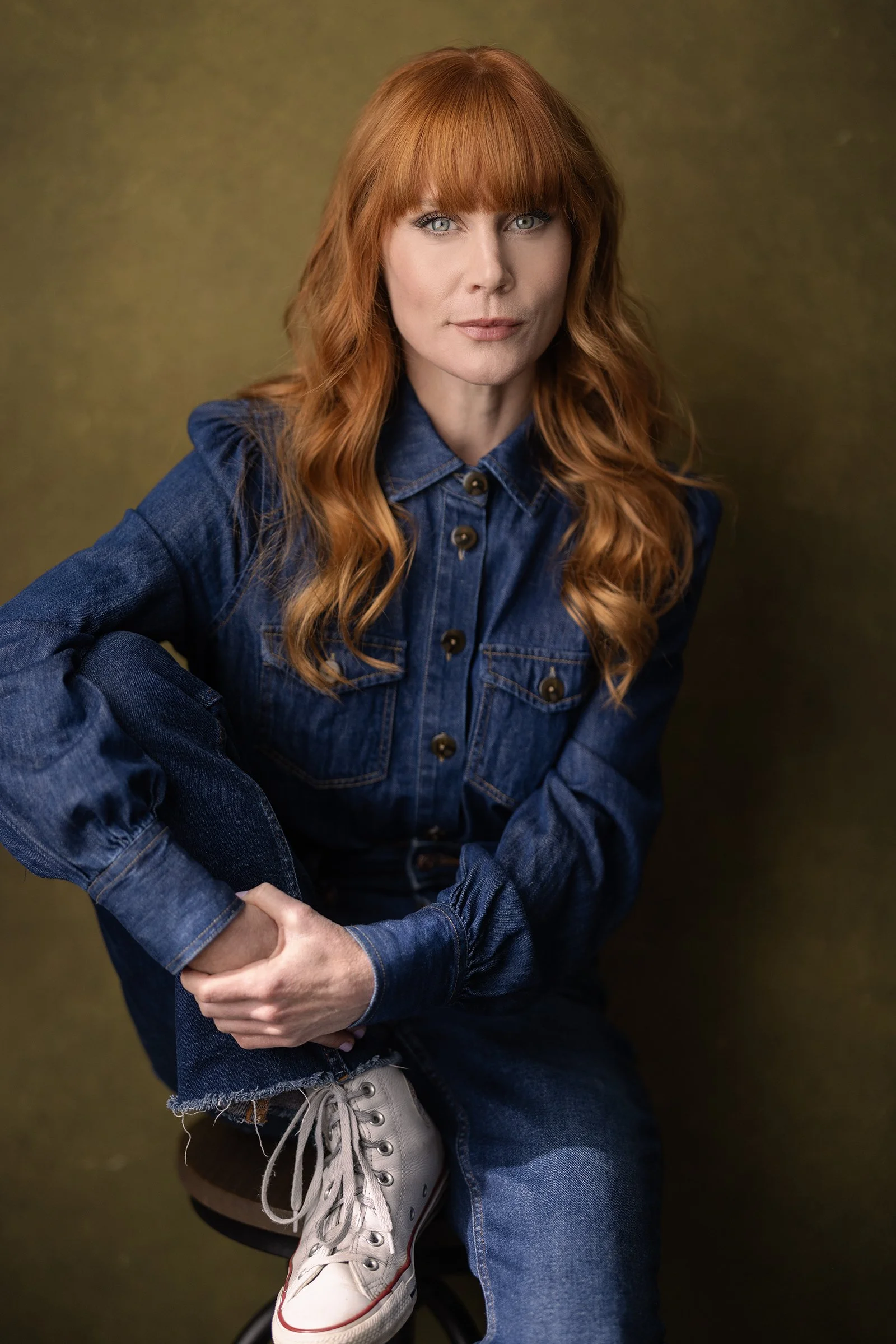 New Zealand actor Michelle Blundell photographed by Andi Crown Photography. She is looking to camera with a warm smile and long red hair,  wearing a denim shirt and jeans with white Converse Chuck Taylors