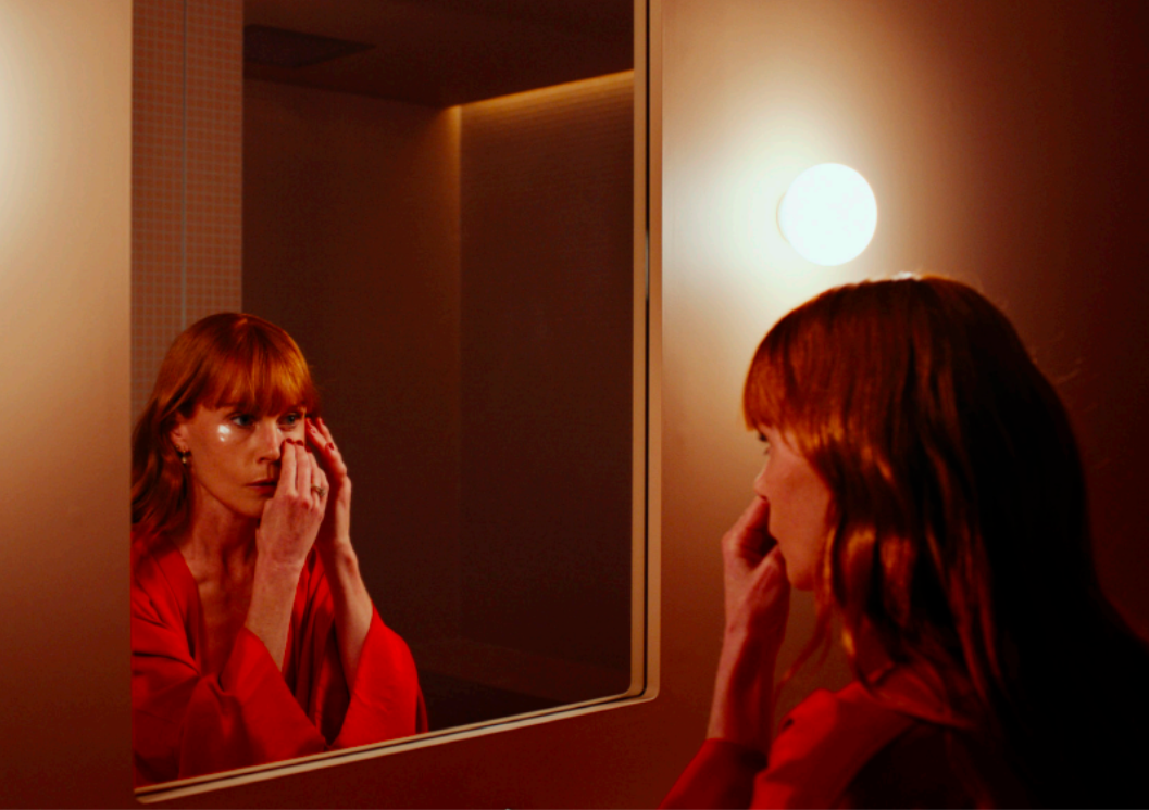 Actor Michelle Blundell in a film still from the New Zealand short film Monologue. Michelle is looking into a mirror in a red dressing gown, applying under eye patches