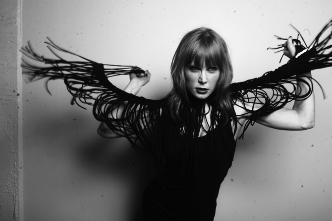 A black and white photograph of actor Michelle Blundell taken by Michelle Hyslop, with art direction from Kim Band. Michelle is wearing black singlet and black frayed scarf