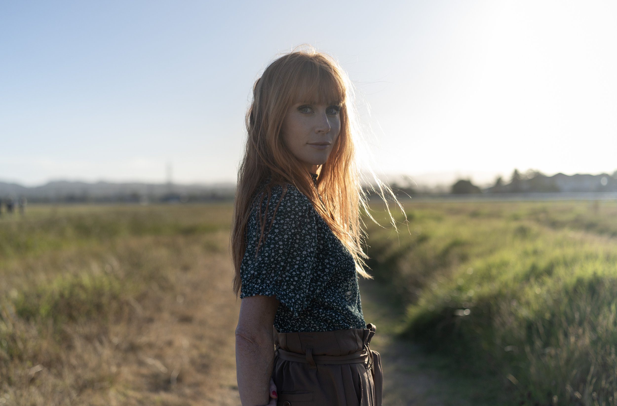 New Zealand actor / actress Michelle Blundell photographed by Emma Cosgrave looking to camera in a field with her hands behind her back