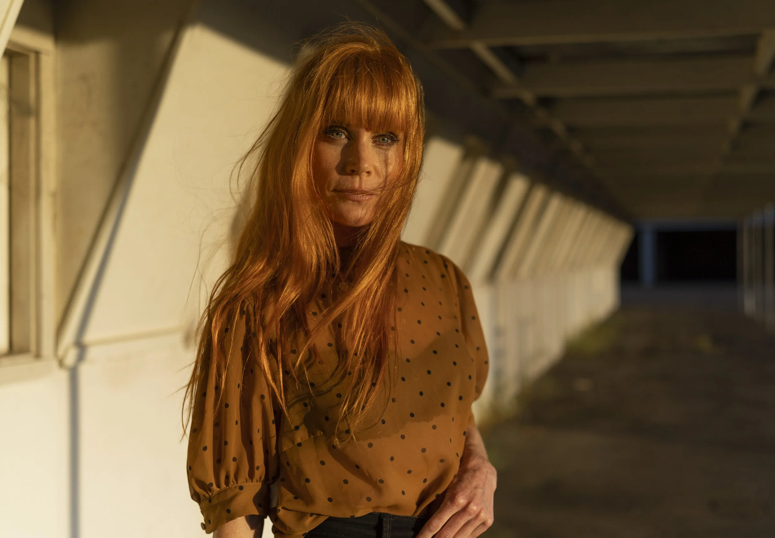 New Zealand actor Michelle Blundell photographed by Emma Cosgrave. She is looking to camera with long red hair blowing on her face