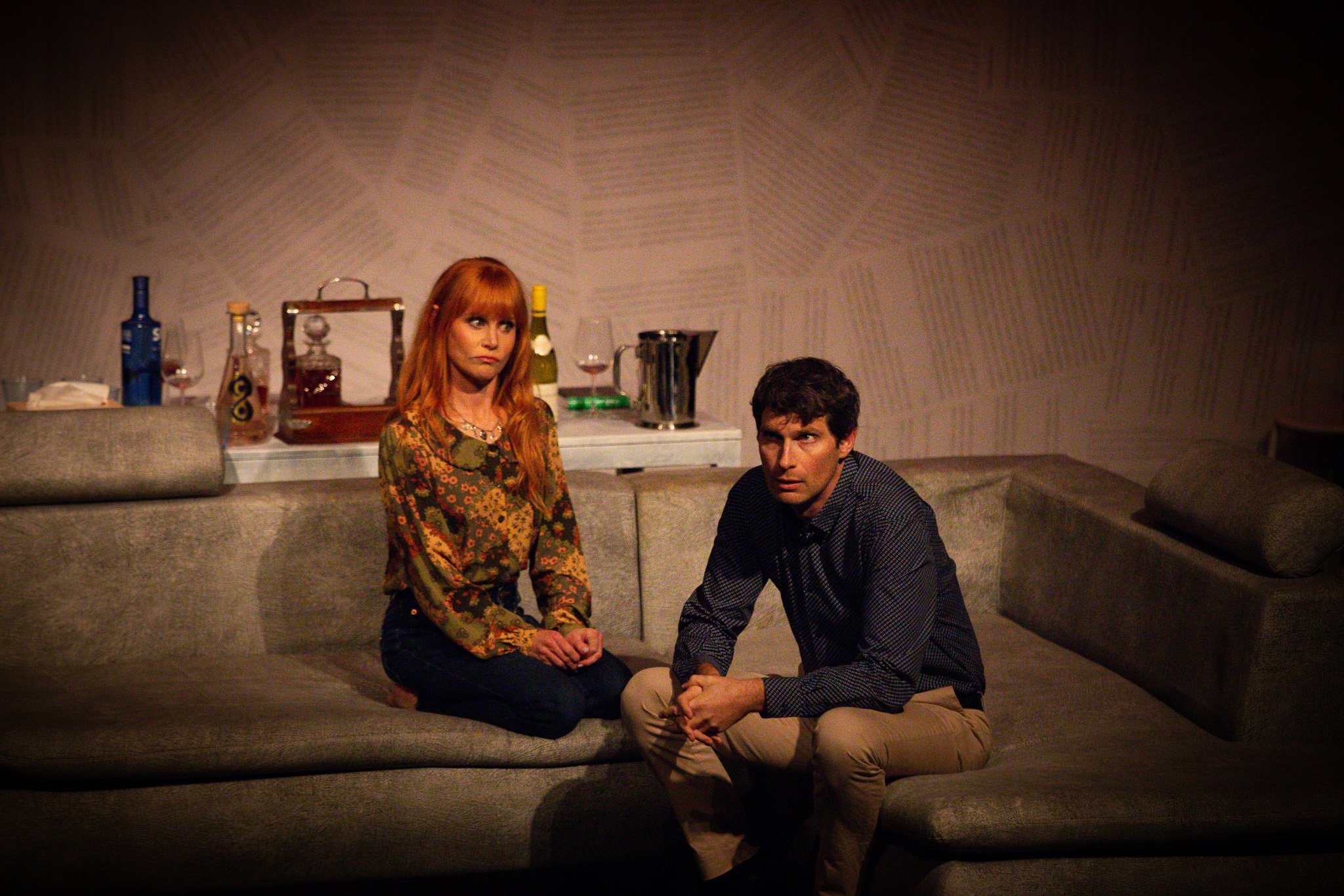 Actors Michelle Blundell and Sam Bunkall in a production still from the New Zealand premiere of Three Little Words. They are sitting closely together on a large beige couch