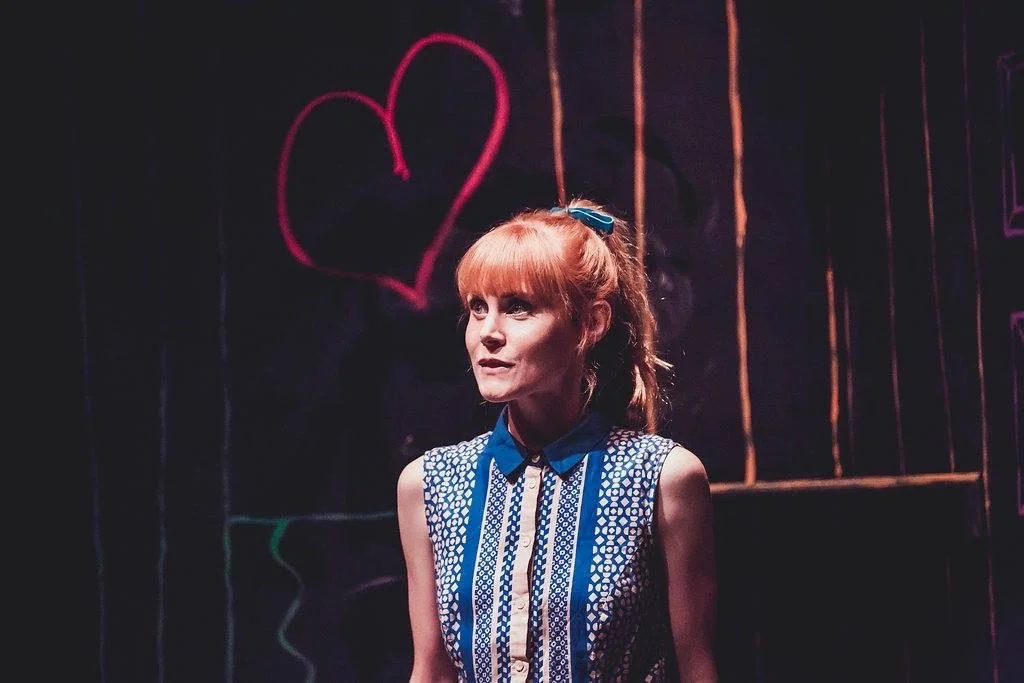 A production still of actor Michelle Blundell as Eliza in The Book of Everything for Silo Theatre. Michelle has her hair in a ponytail and is wearing a blue patterned dress
