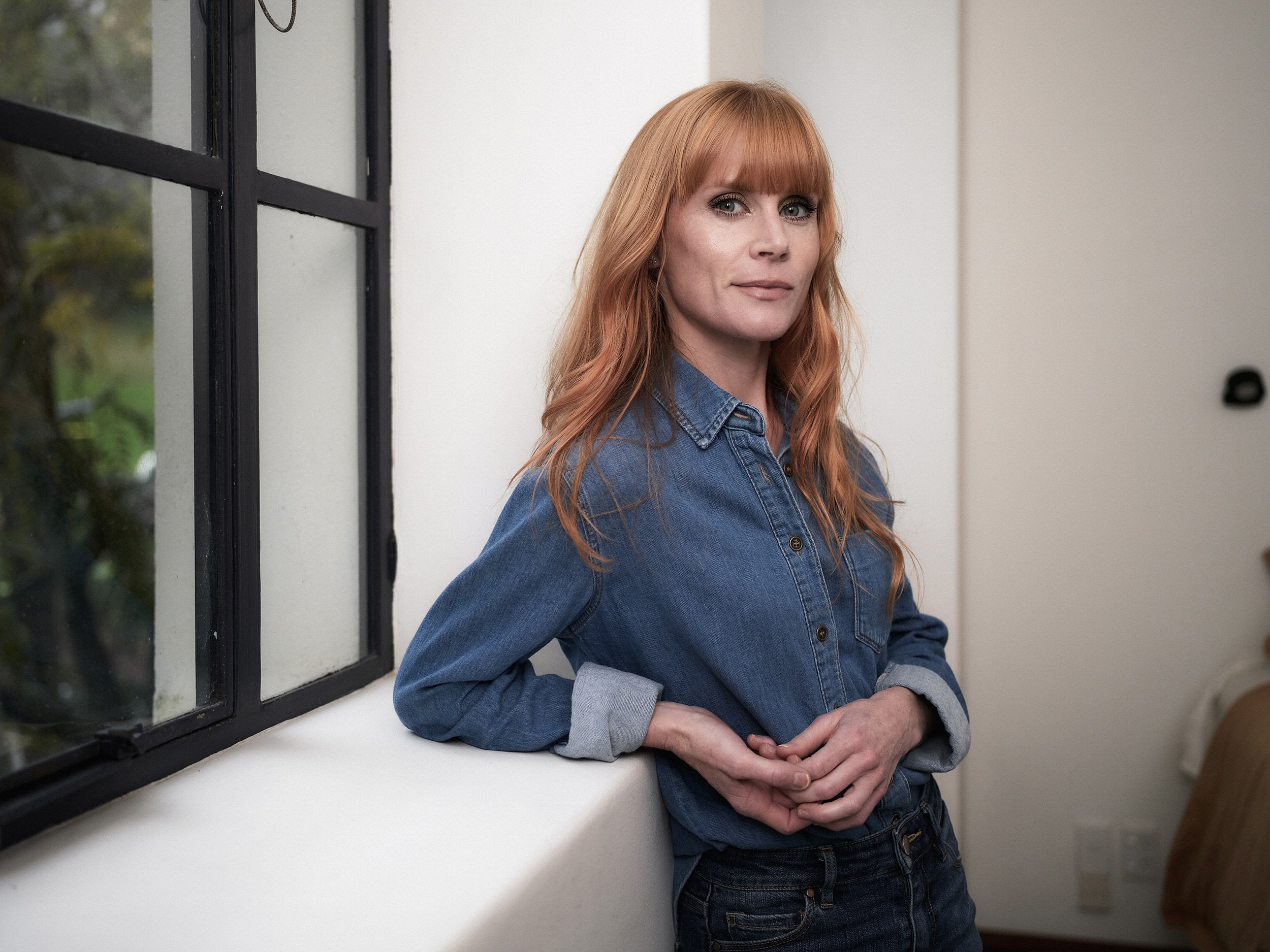 New Zealand actor / actress Michelle Blundell standing by a window wearing a denim shirt and jeans. Photographed by Zico O'Neill-Rutene