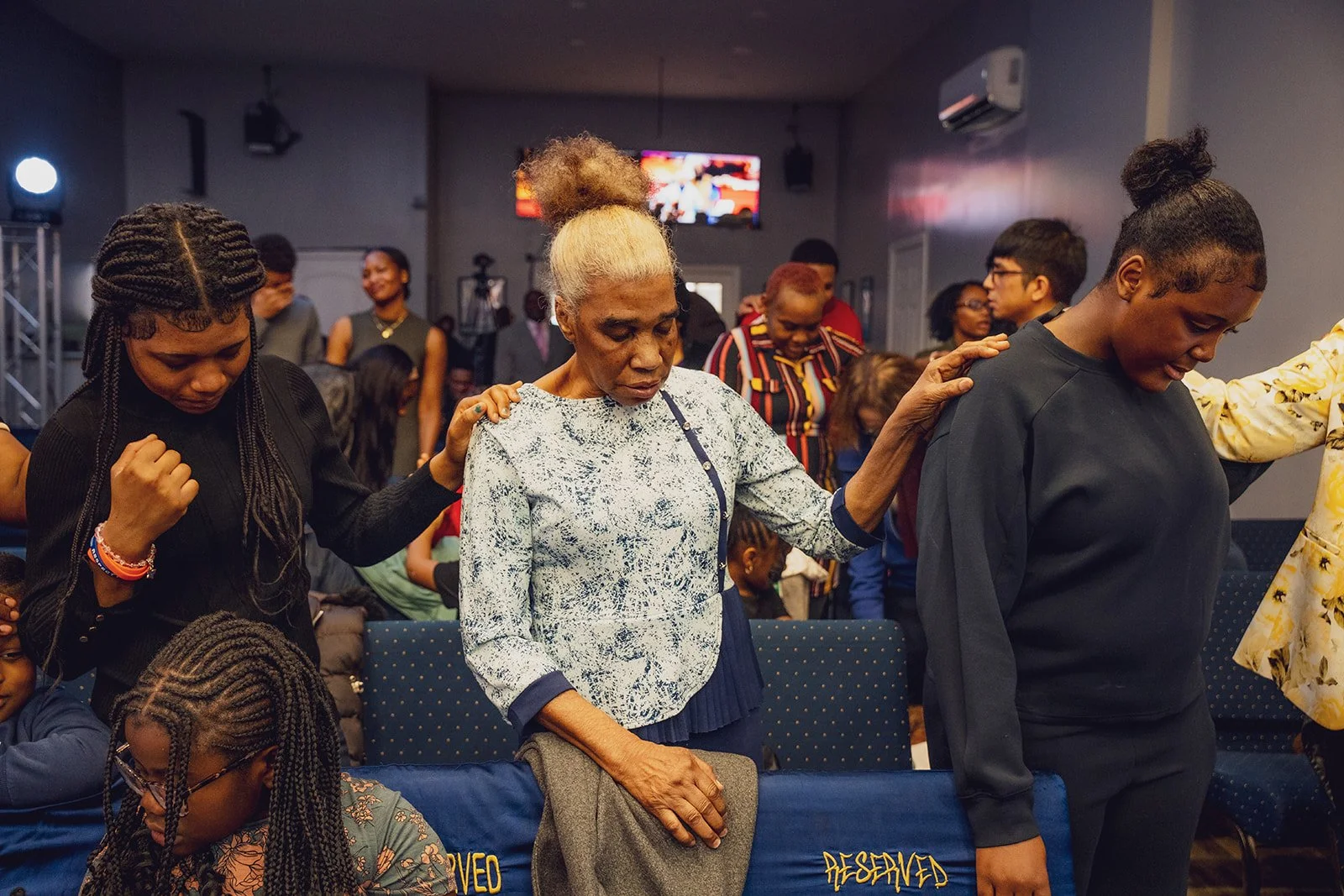 Group of people praying with their eyes closed in a church or prayer setting.