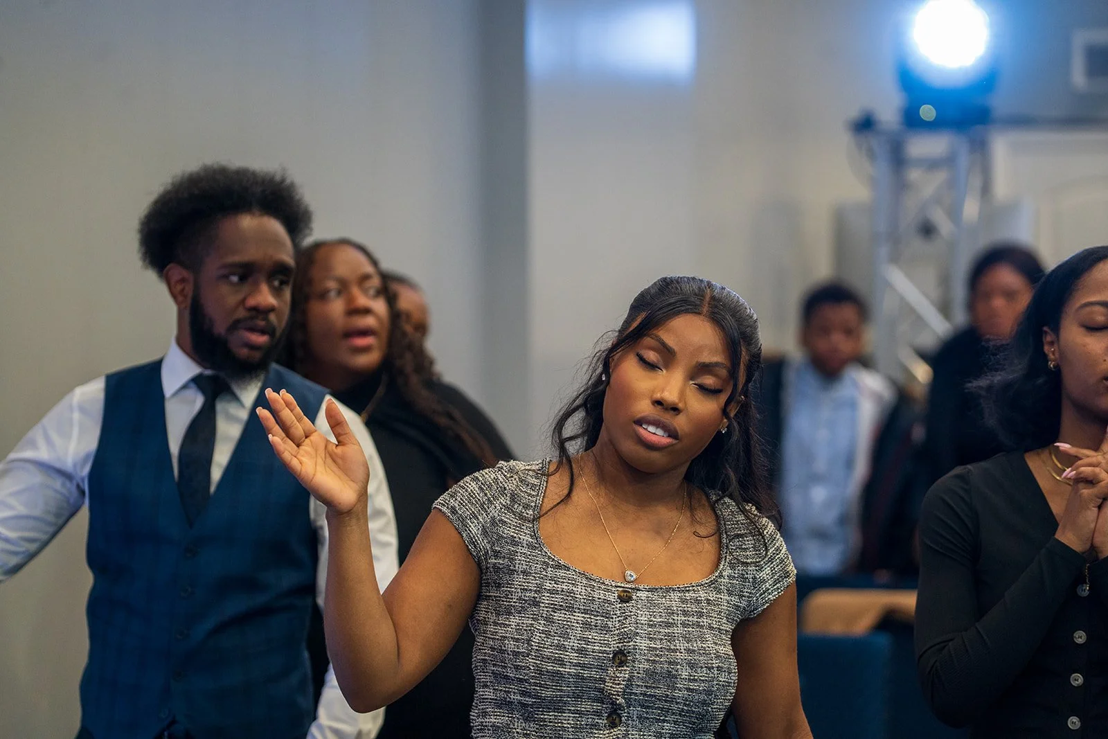 A diverse group of people standing in prayer or meditation with closed eyes, in a church or spiritual setting.