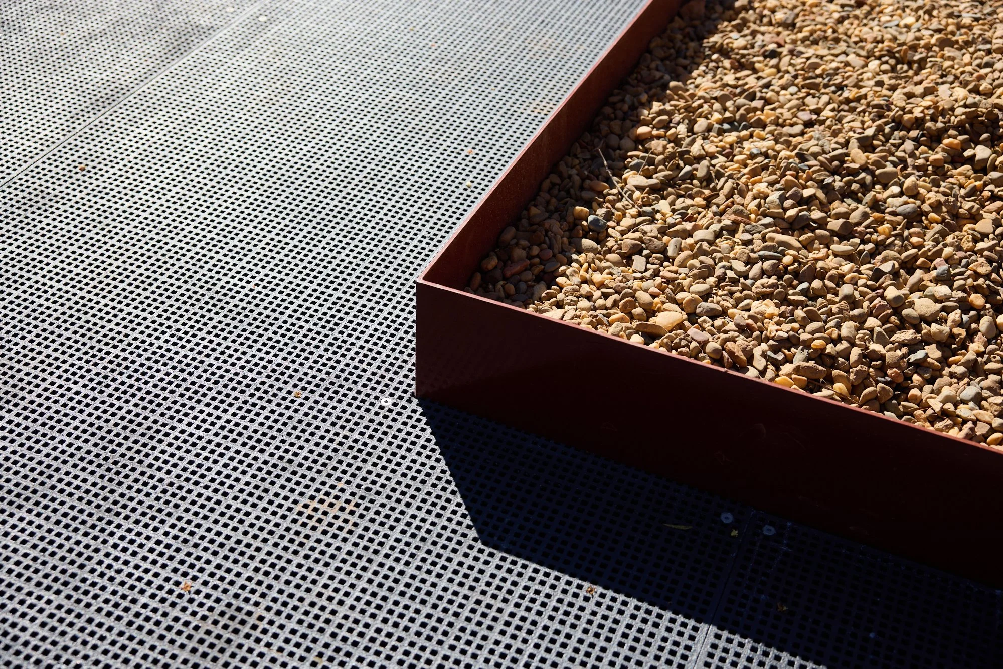 Close-up of a gravel-filled metal planter box on a textured gray outdoor surface.