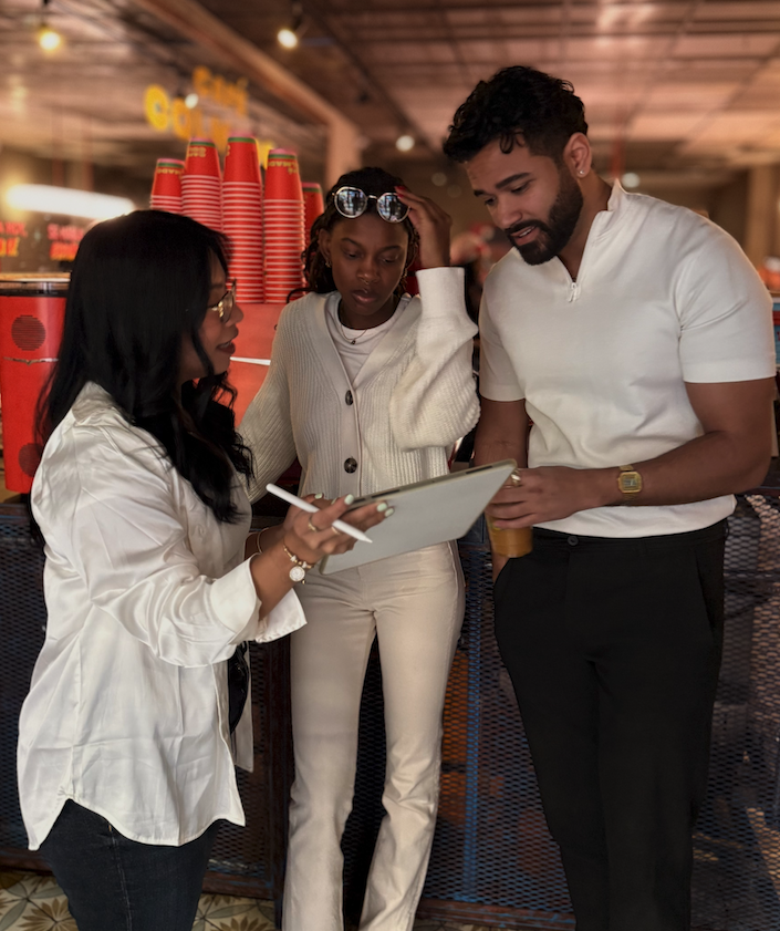Three diverse professionals reviewing digital content on a tablet in a casual indoor setting, with one woman demonstrating insights to a man and another woman.