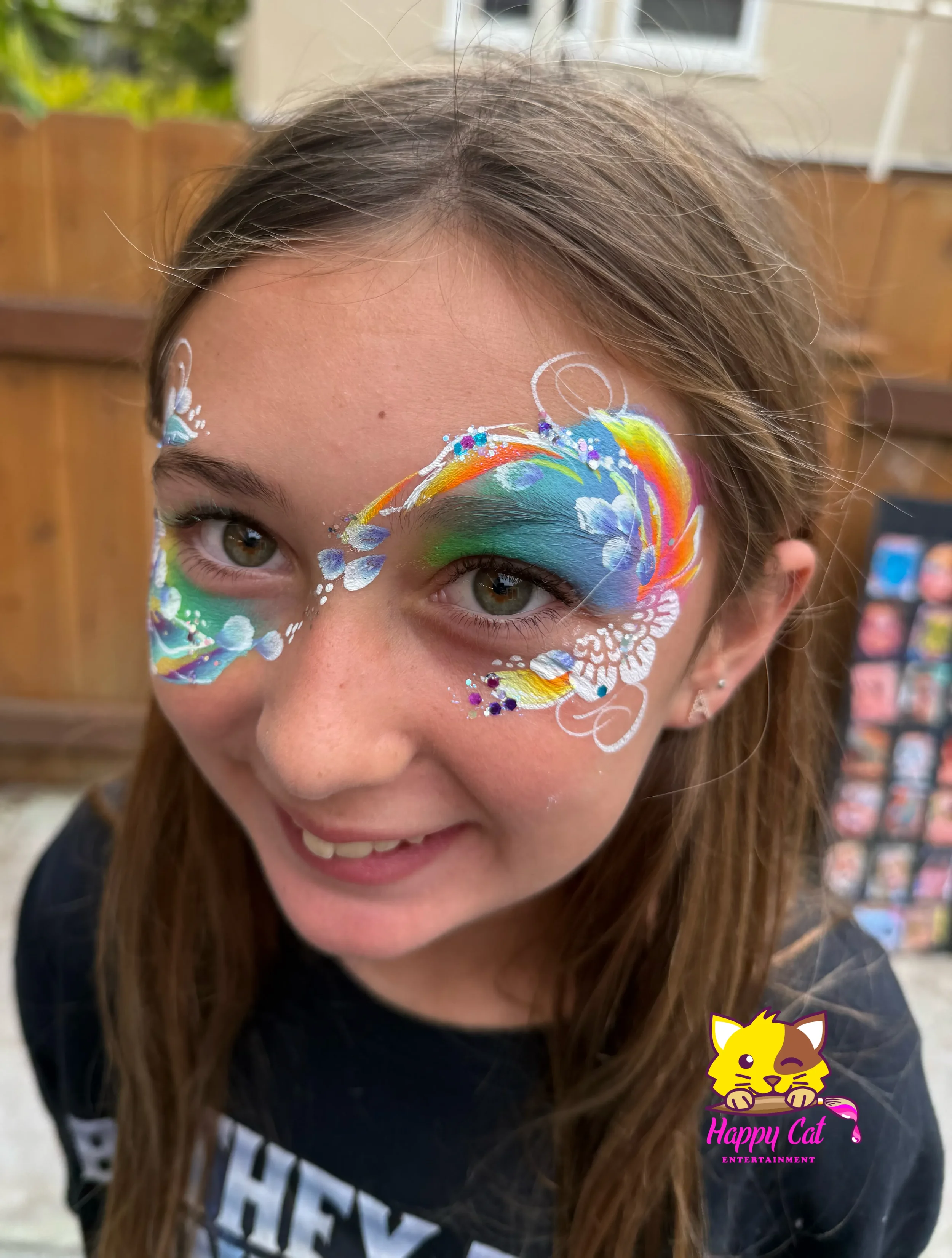 A girl with face paint of a colorful butterfly design around her eyes, featuring blue, green, yellow, white, and purple colors, with white and purple accents.
