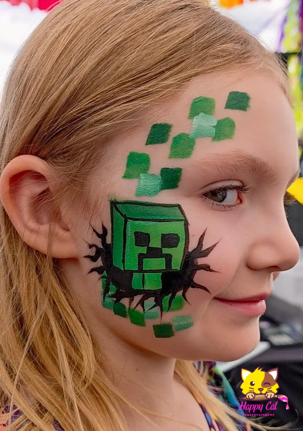 A young girl with face paint of a green Creeper from Minecraft on her cheek and forehead, surrounded by green pixels.