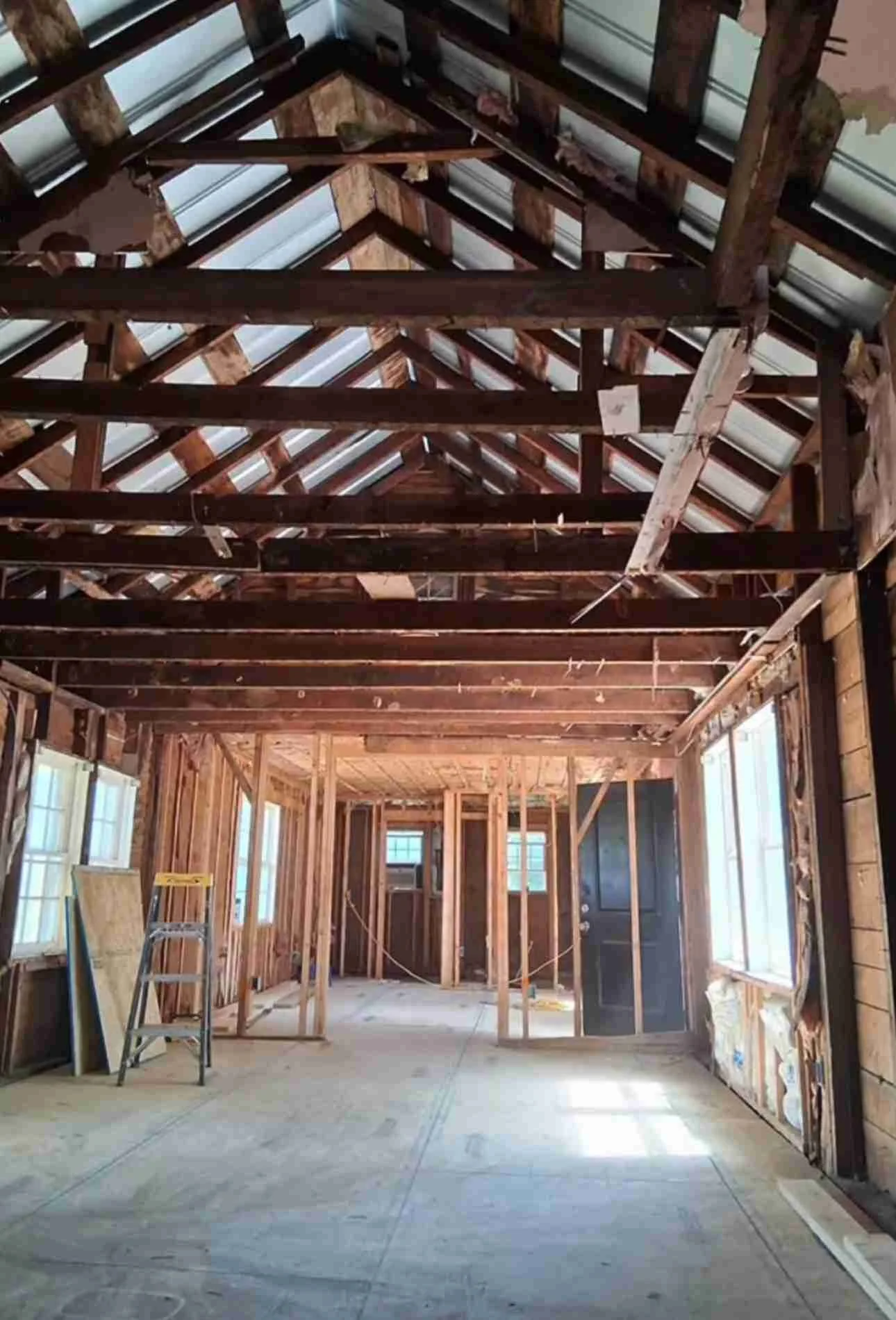 Interior of a house under construction with exposed wooden framing, a partially completed roof, and a plywood floor.
