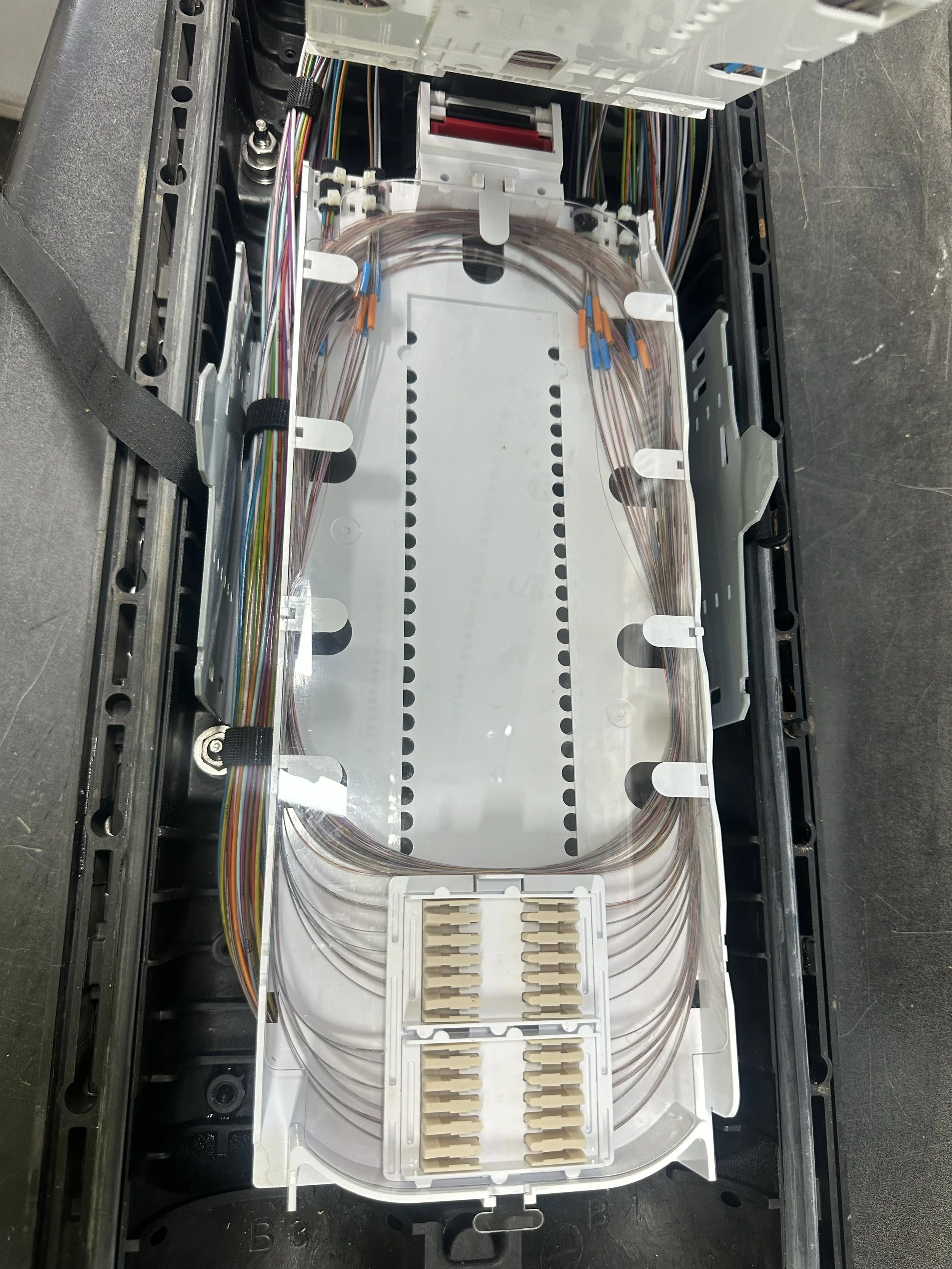 Inside view of a fiber optic splice closure with multiple color-coded fiber optic cables arranged neatly inside.
