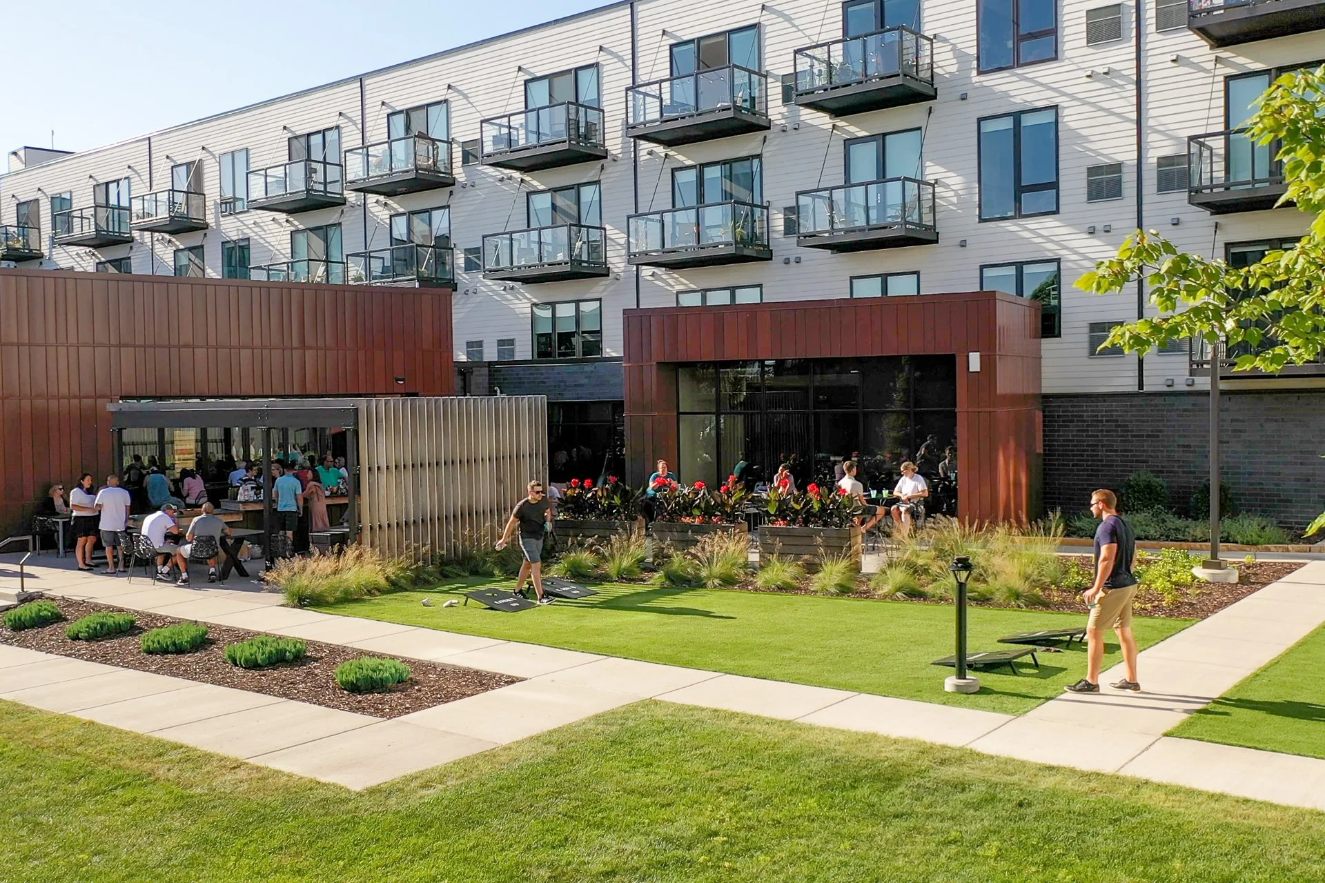 Residents enjoying outdoor amenities at an apartment complex with a lawn, garden beds, and a building with balconies.