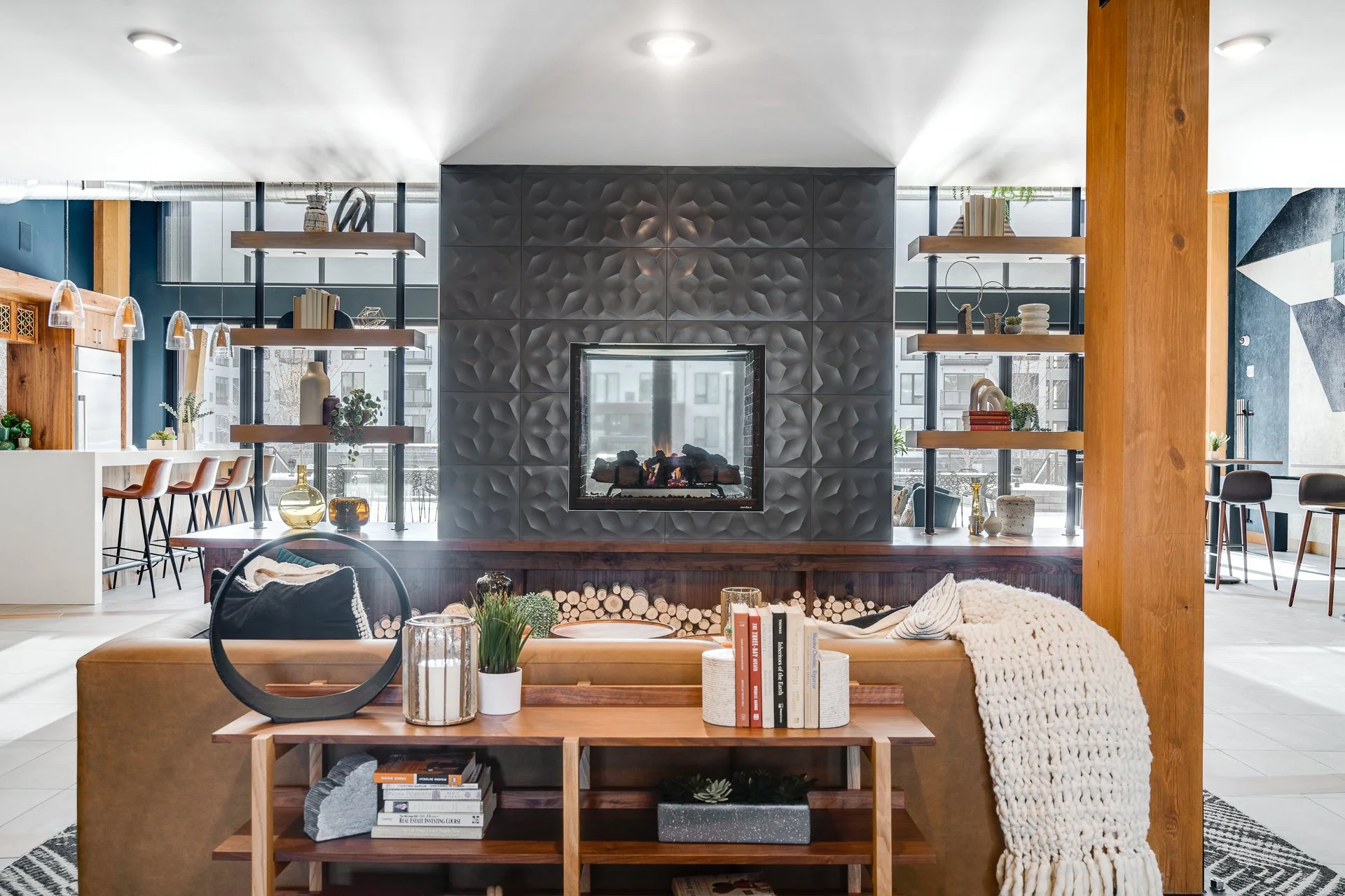 Modern living room with a fireplace, decorative shelves, plants, books, and cozy seating area with a throw blanket.