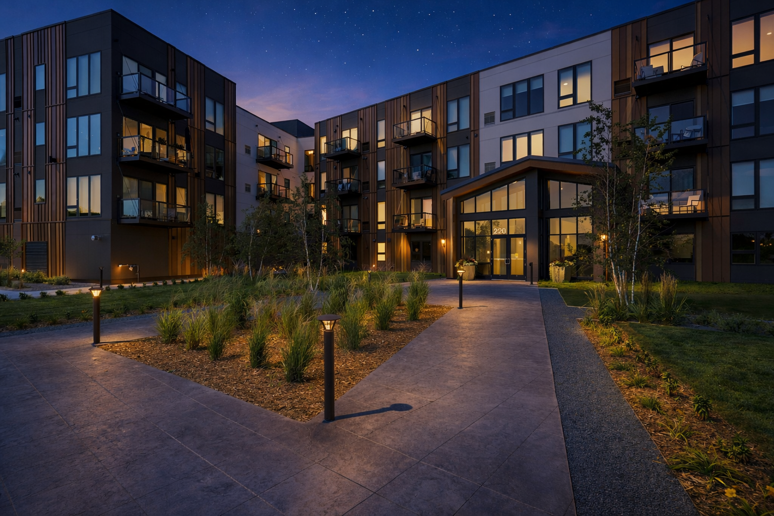 Modern apartment complex at evening with illuminated balconies, landscaped pathway, garden, and pathway lights under a starry sky.