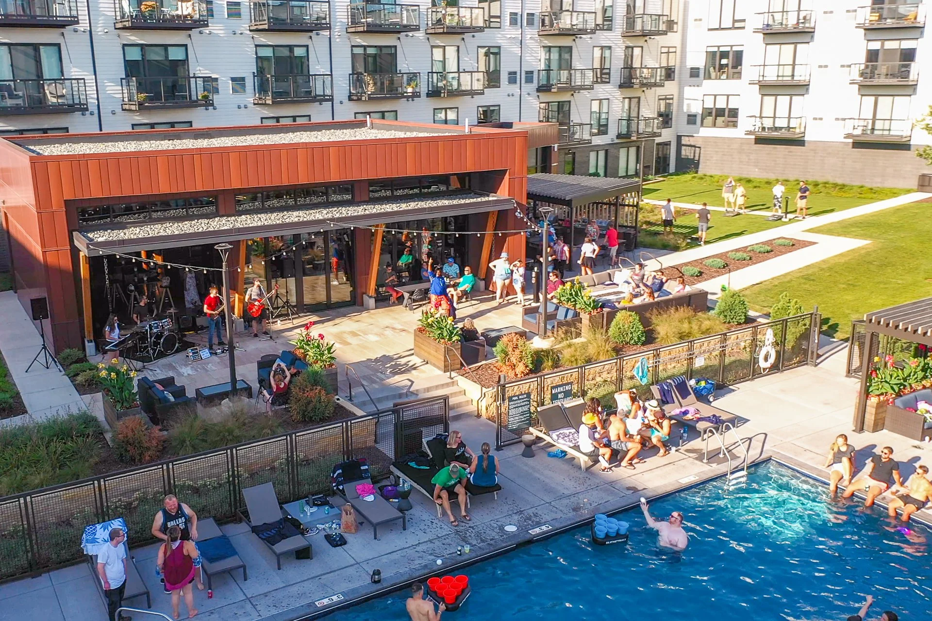 People enjoying a poolside gathering with live band performance at an outdoor patio of a modern apartment complex.