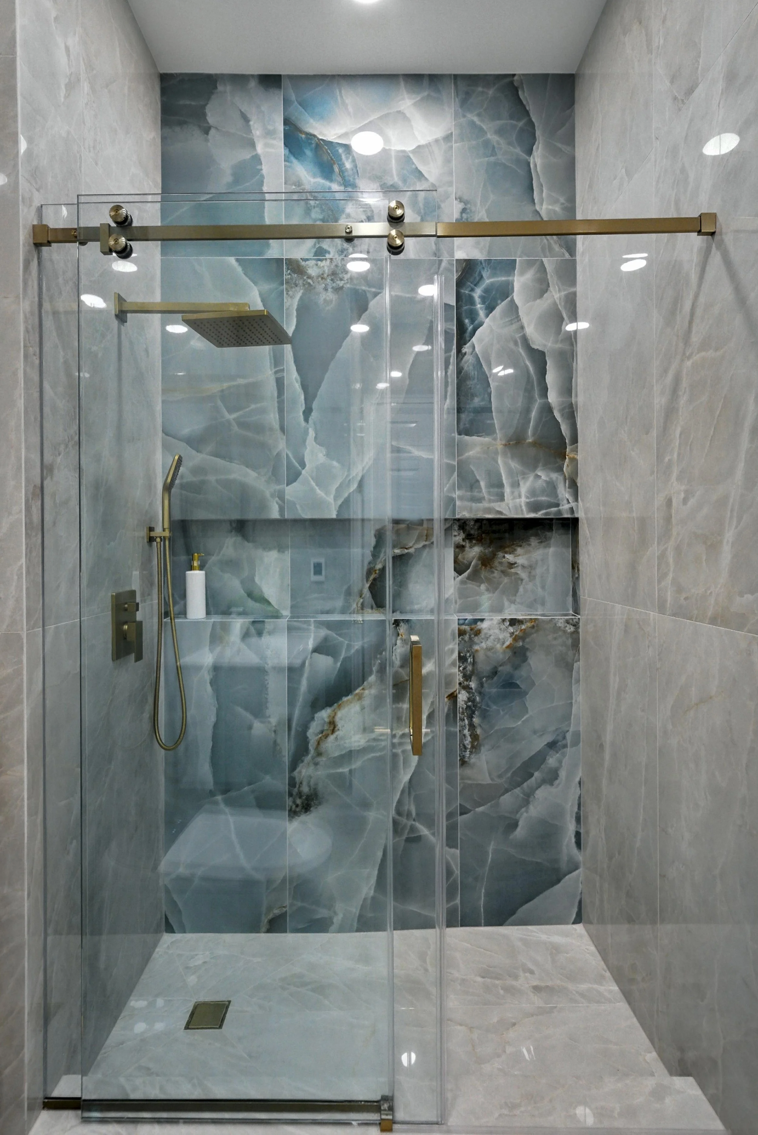 Modern walk-in shower with blue and gray marble tiles on the accent wall, glass doors, a rainfall showerhead, and a handheld shower fixture.