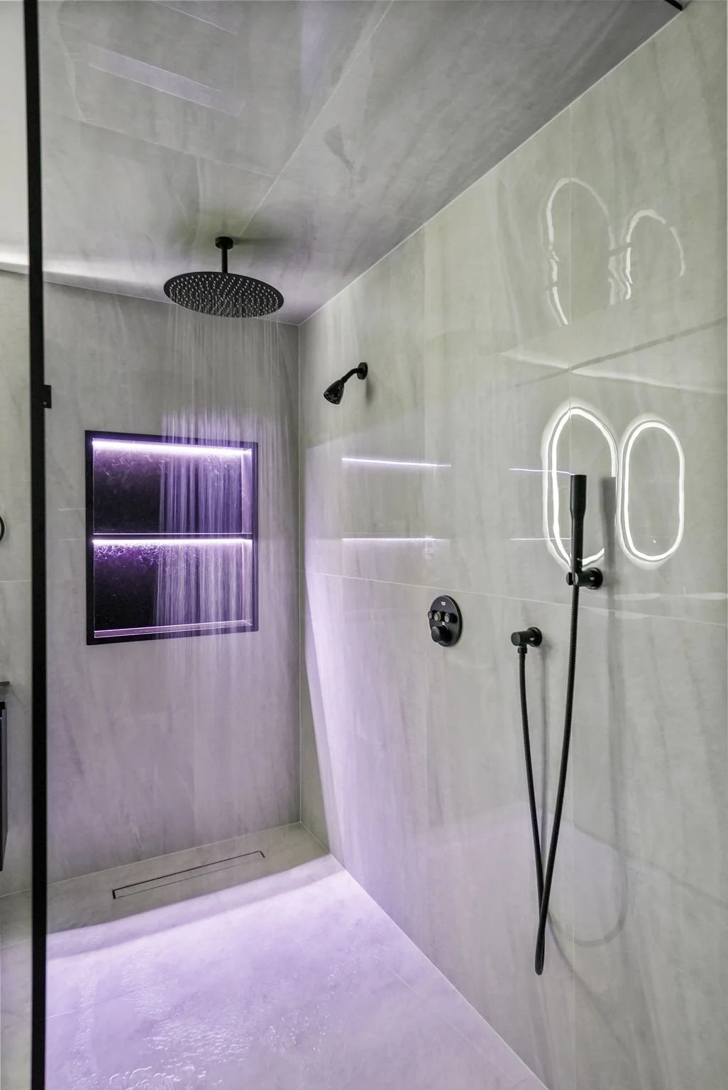 Modern shower with large rainfall showerhead, hand-held shower, black fixtures, and purple LED-lit shelf