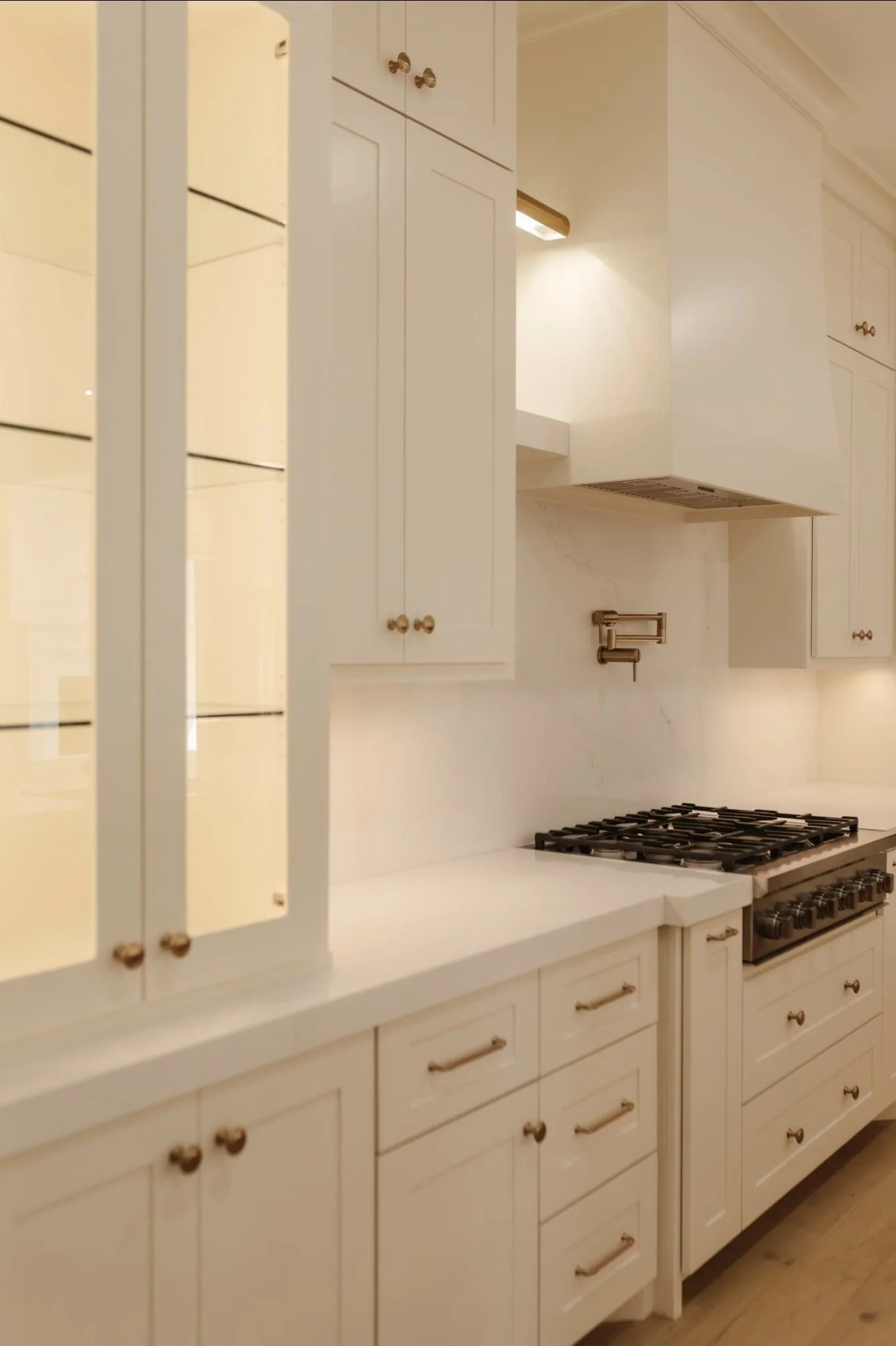 White kitchen with cabinets, drawers, gas stove, and a metallic pot filler faucet on the wall.