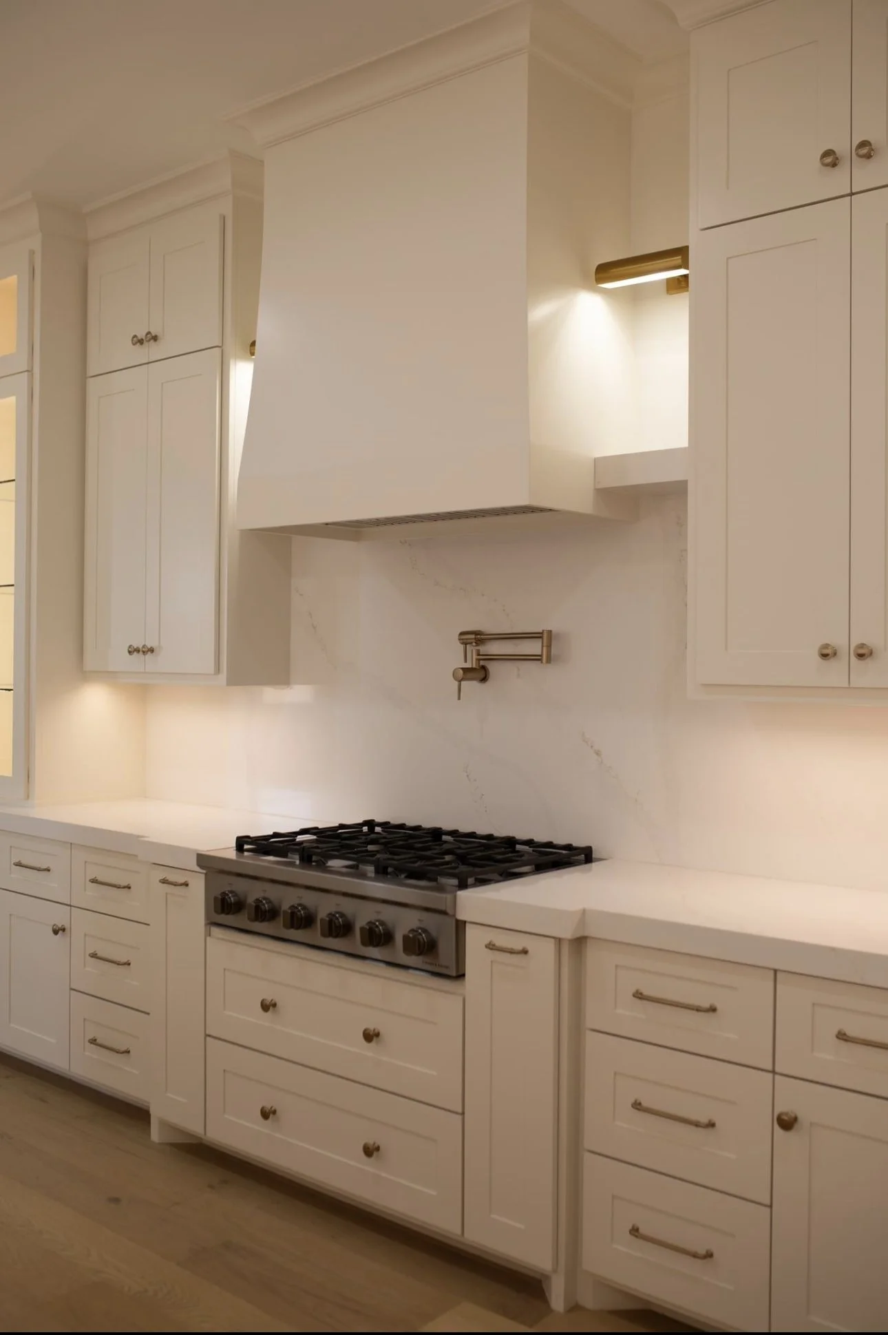 White kitchen with cabinets, a gas stove, and a range hood.