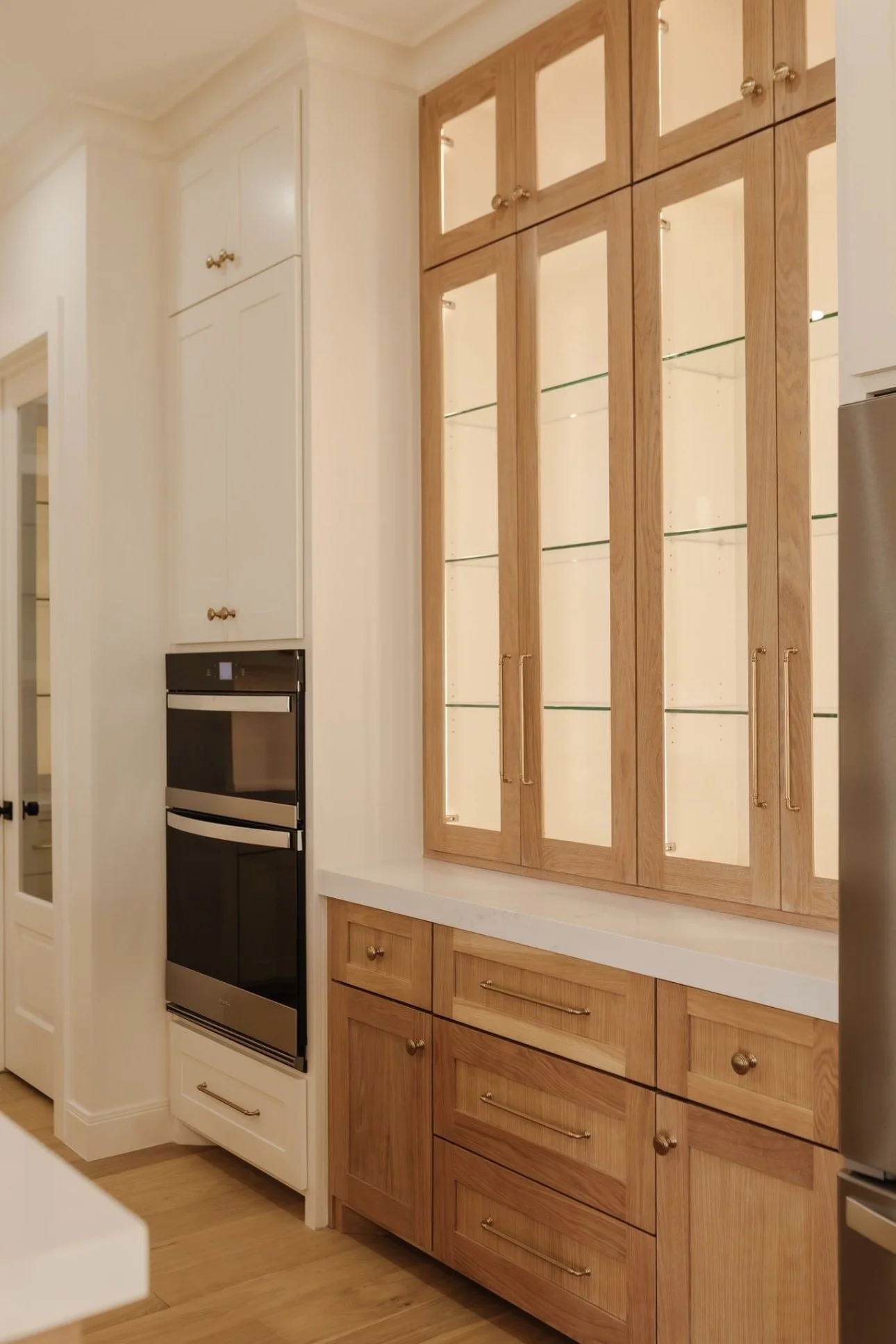 Kitchen corner with wooden and white cabinetry, built-in oven, glass-front cabinets, and a wooden countertop.