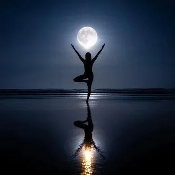 A person practicing yoga on the beach at night with the full moon in the background.