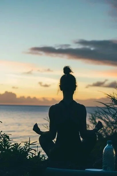 Silhouette of a woman meditating by the ocean at sunset.