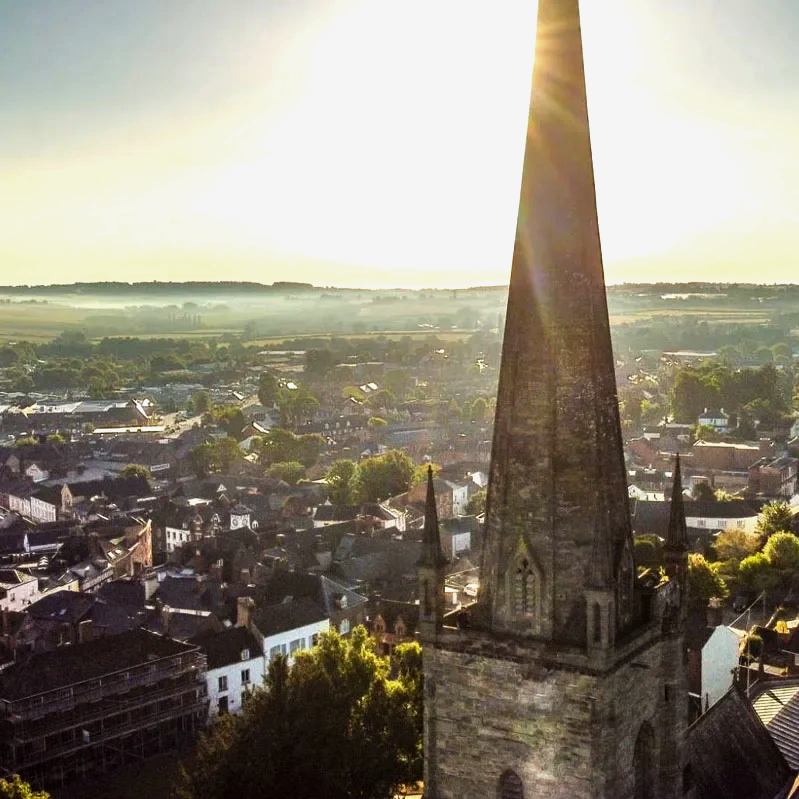 Aerial view of a town with a prominent church steeple in the foreground, sunlight shining over the town and surrounding countryside.