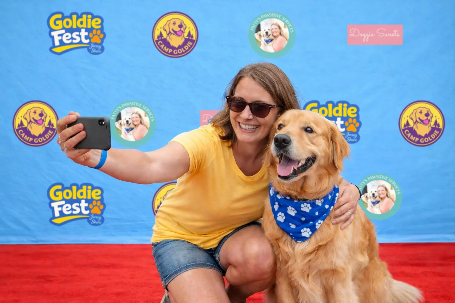 Woman taking a selfie with her golden retriever at Goldie Fest, with event banners in the background.