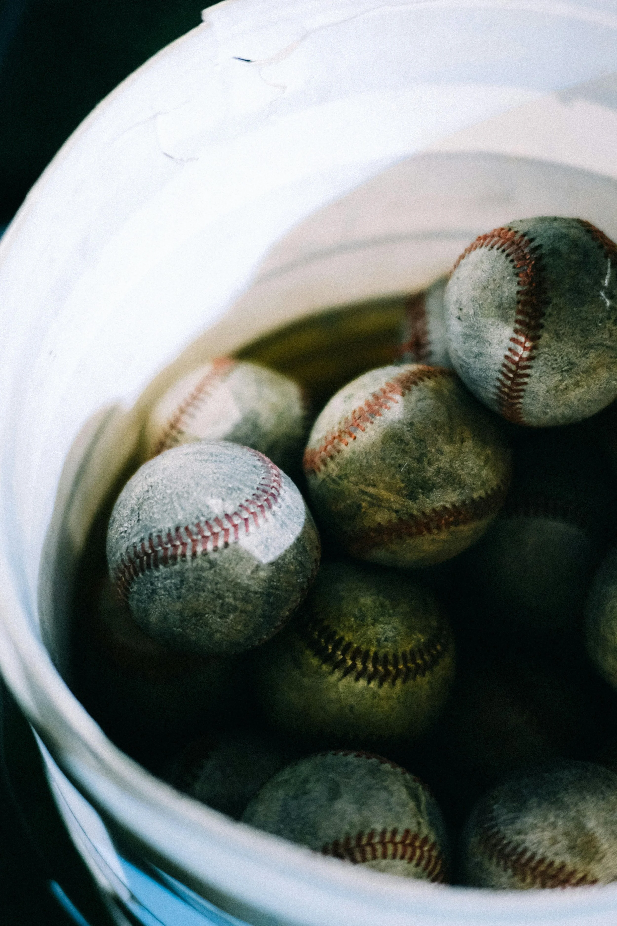 A close-up of a white bucket filled with used baseballs showing dirt and wear.