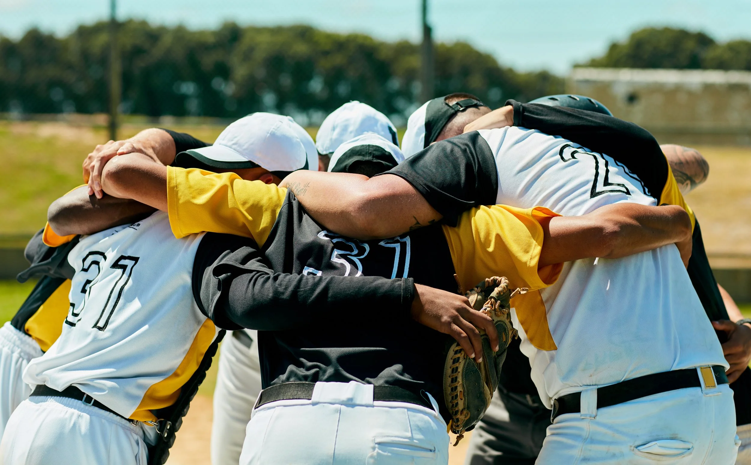 A group of baseball players in team uniforms huddled together in an embrace on the field.