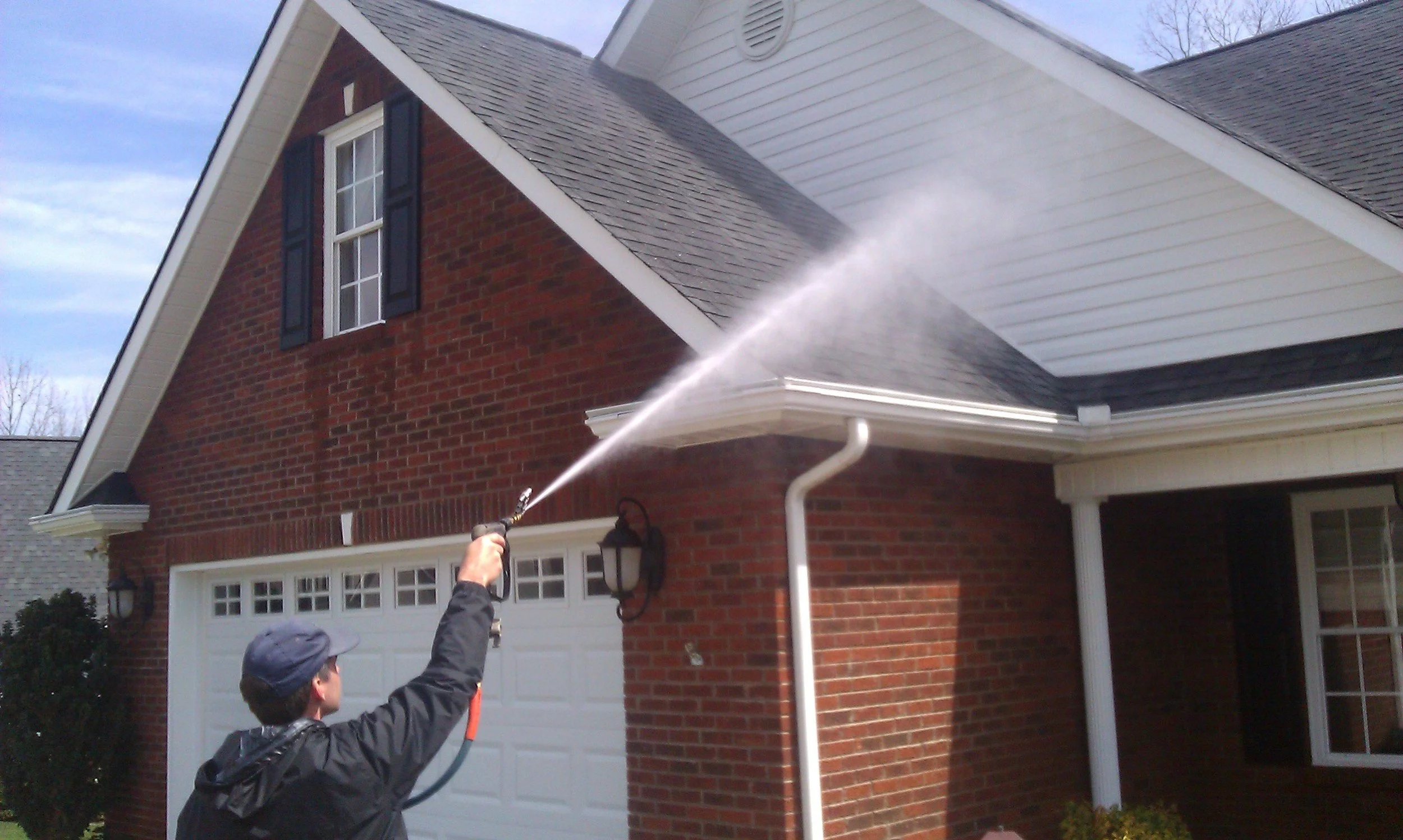 Person pressure washing the roof of a house with a garden hose.