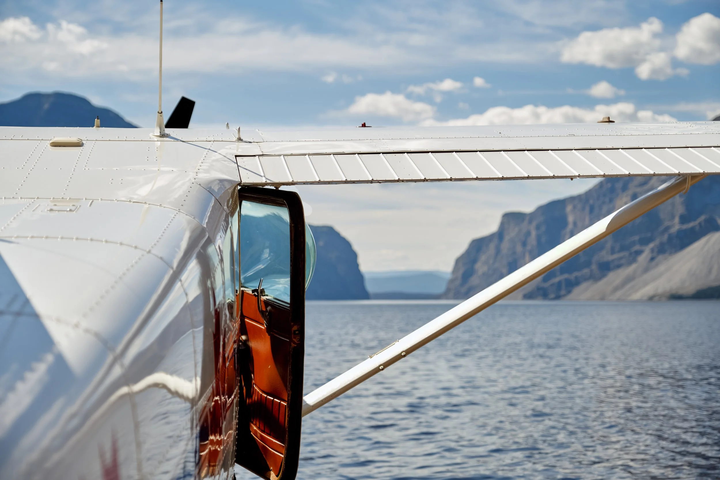Close-up of an aircraft's wing and a section of the fuselage against a backdrop of water and mountains.