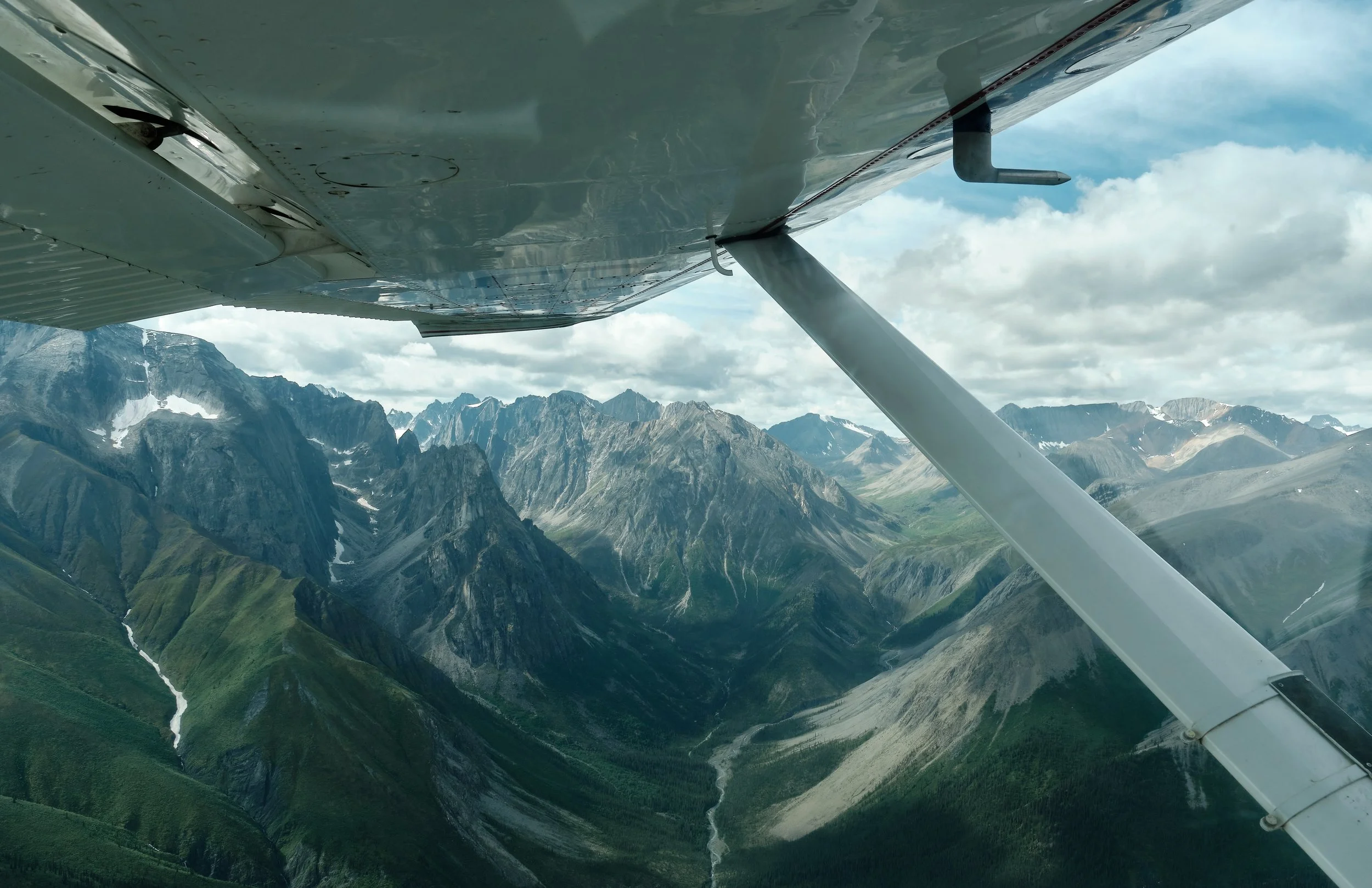 View of rugged mountain range taken from an airplane in flight with part of the wing visible.