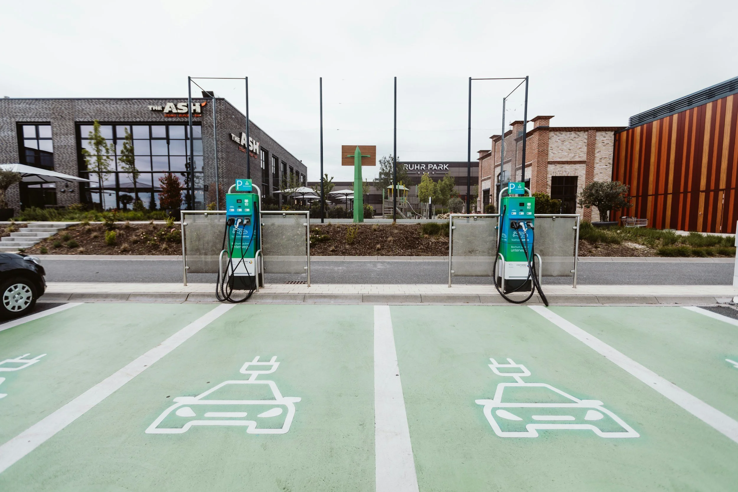 Electric vehicle charging station in a parking lot in front of modern commercial buildings.