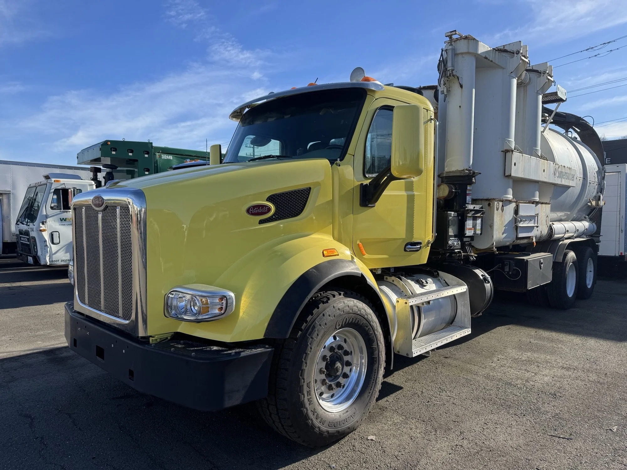 Freshly painted yellow Peterbilt truck parked outdoors with other trucks in the background and blue sky overhead.