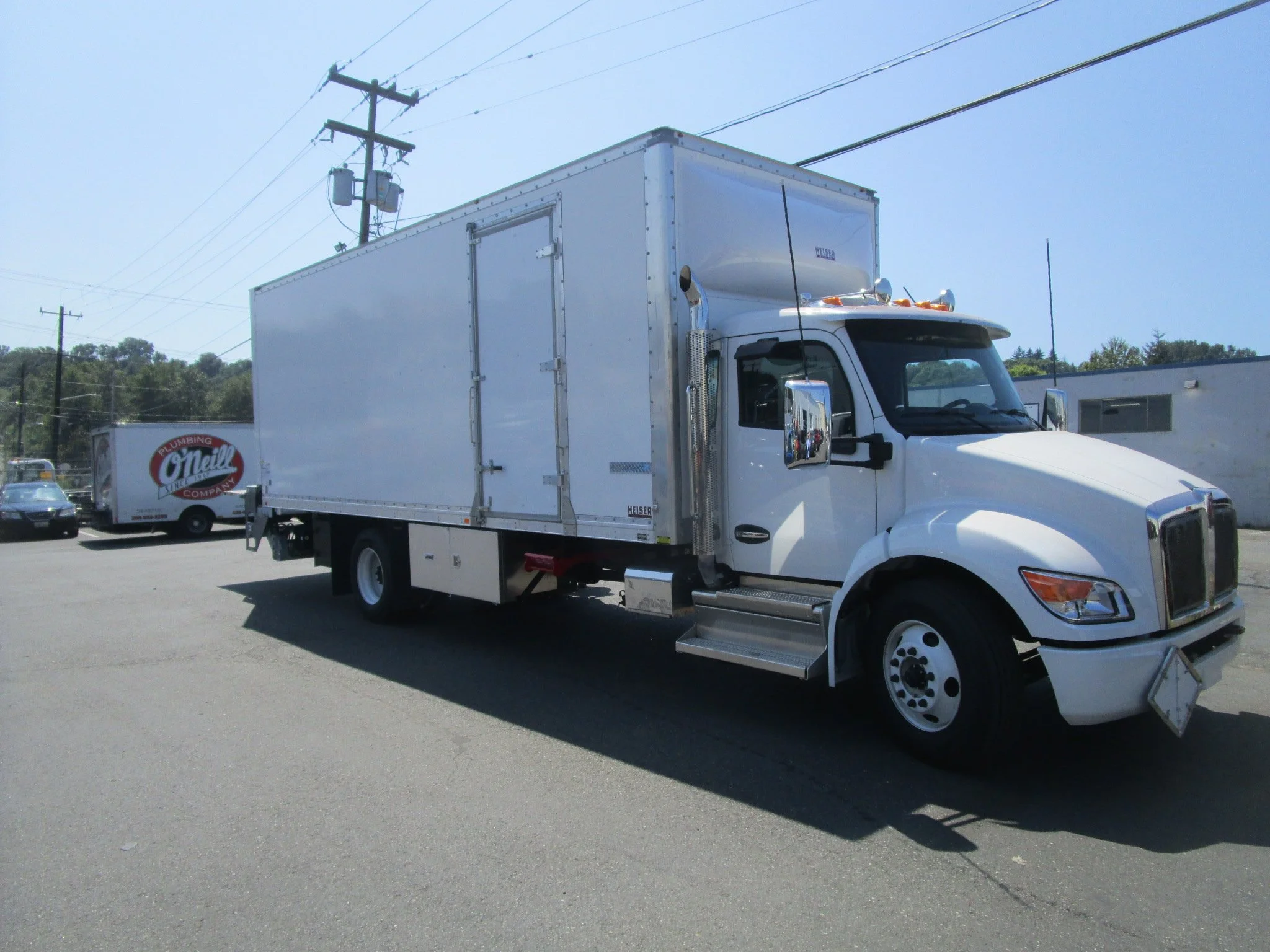 A white box truck with custom cut side door installation parked on a paved lot under power lines.