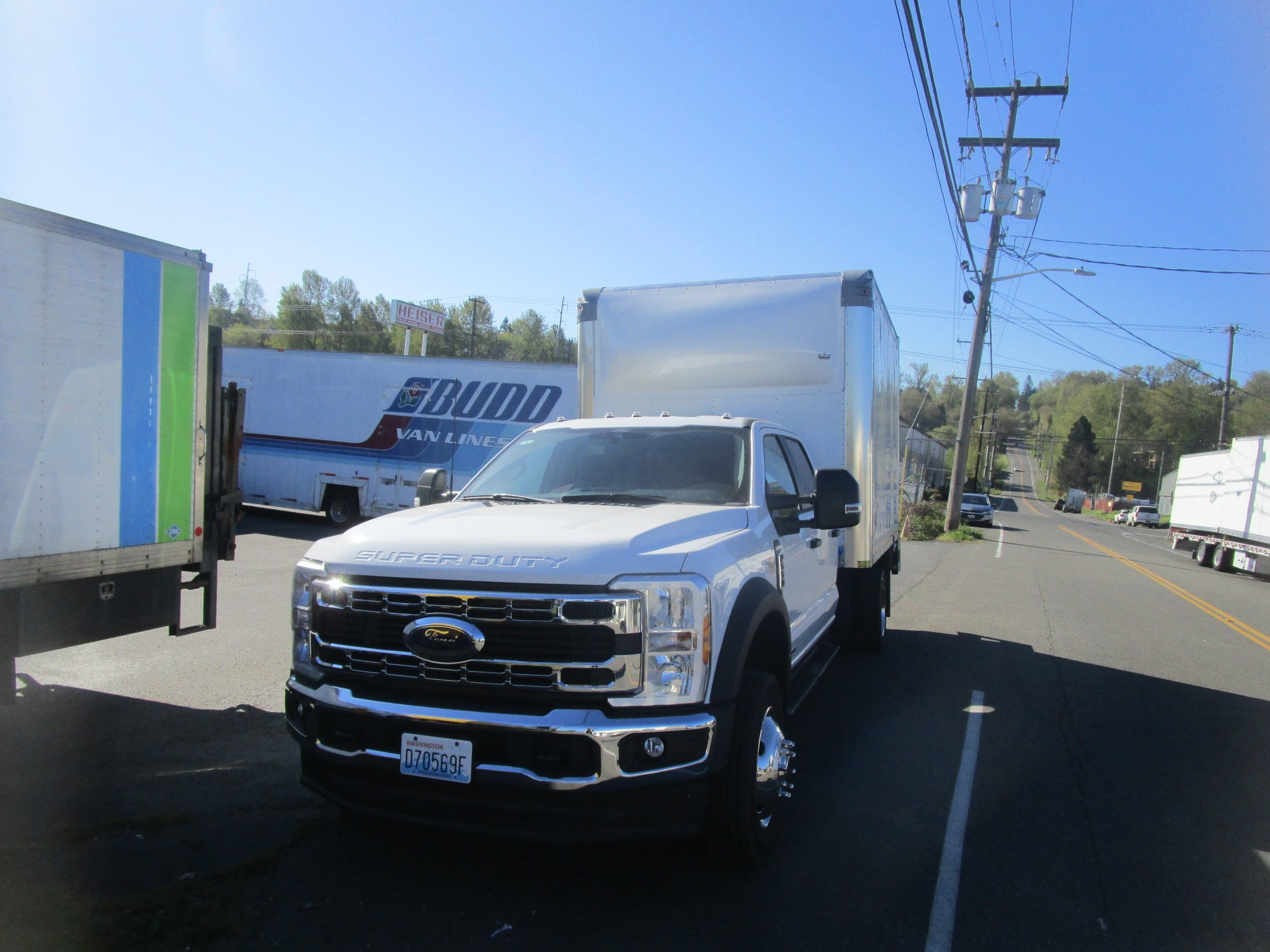 Custom installed white box installed on a Ford Super Duty truck parked on a street, with other trucks nearby and power lines above.