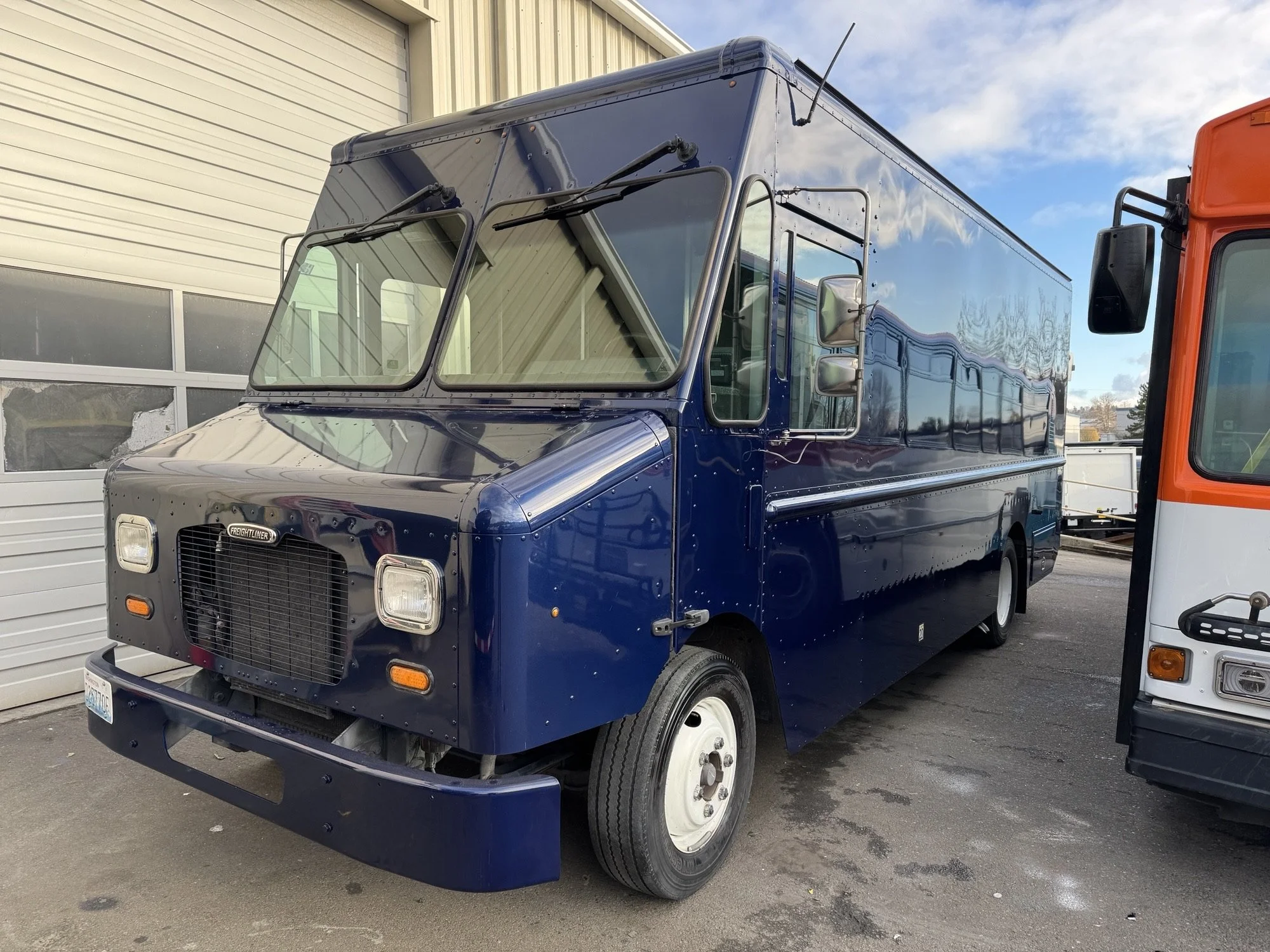 A freshly painted blue delivery truck parked outside the Heiser Body building.