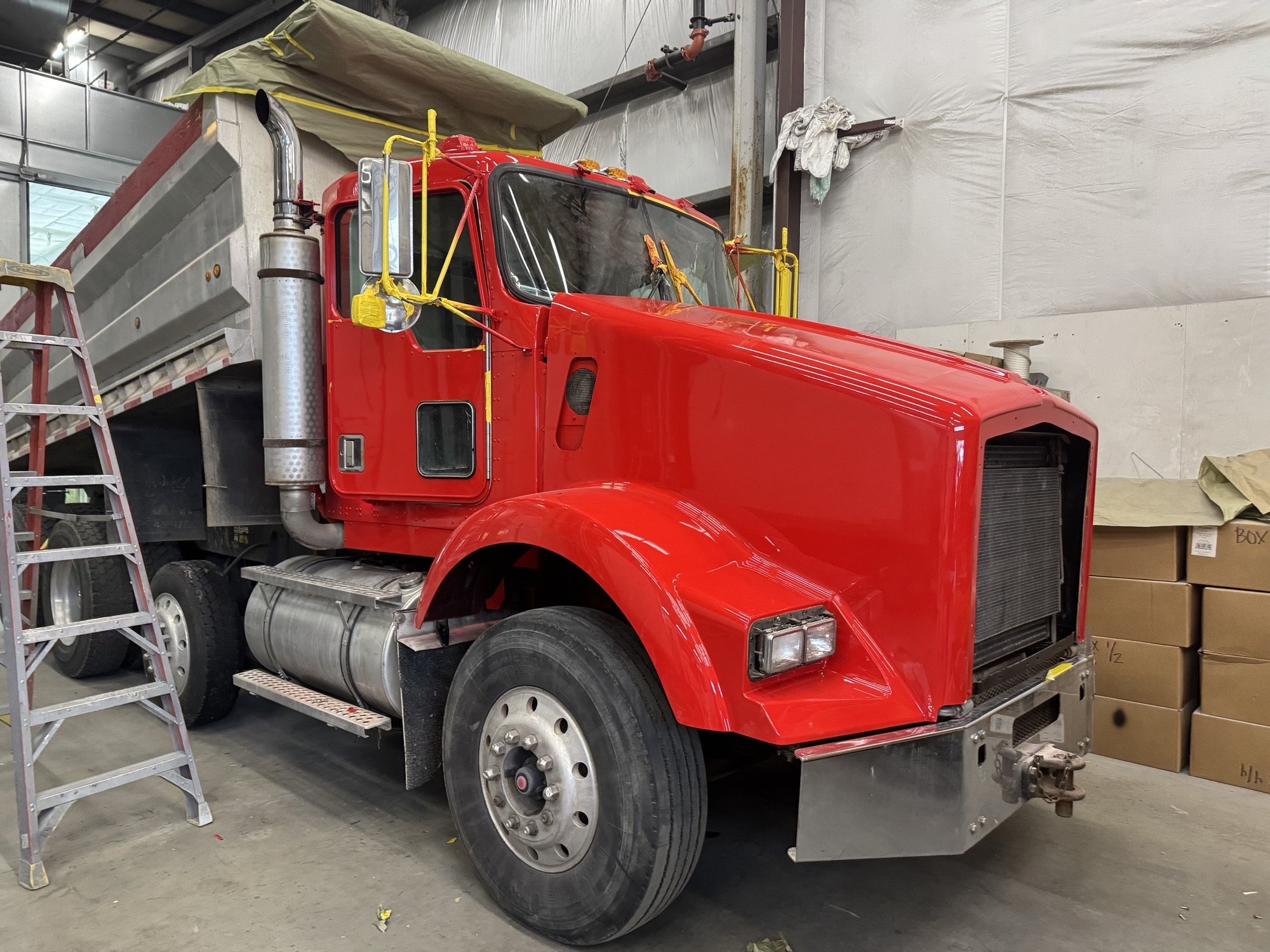A red truck being painted by Heiser Body inside their shop with boxes and a ladder nearby.