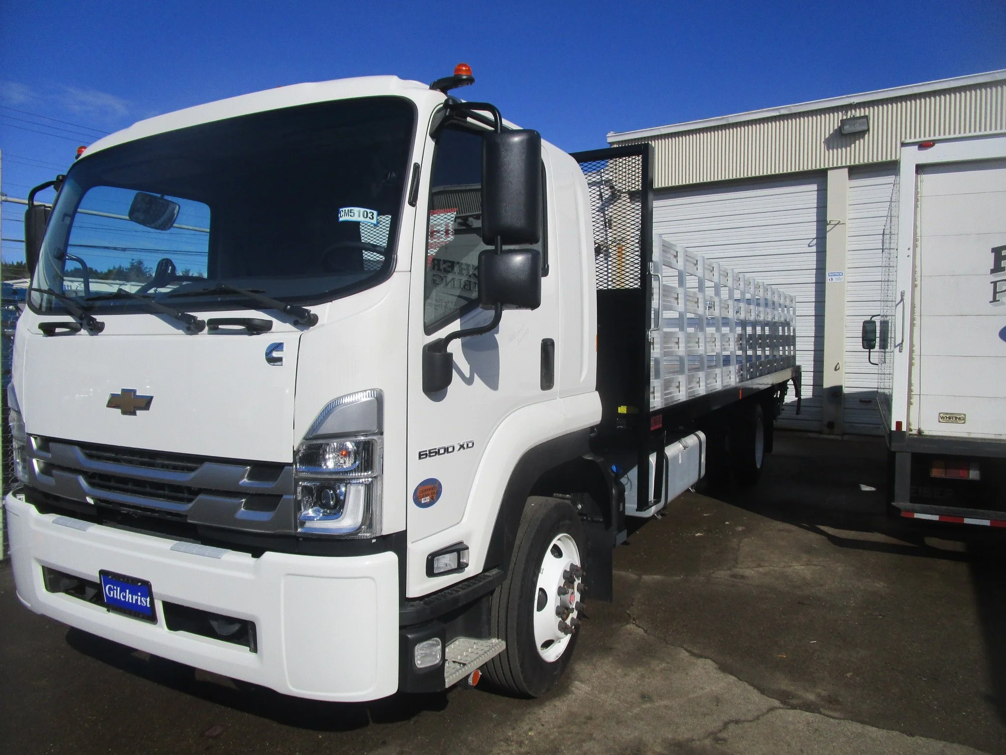 Custom white flatbed van conversion with black accents and prominent front grille parked outside the Heiser Body building.