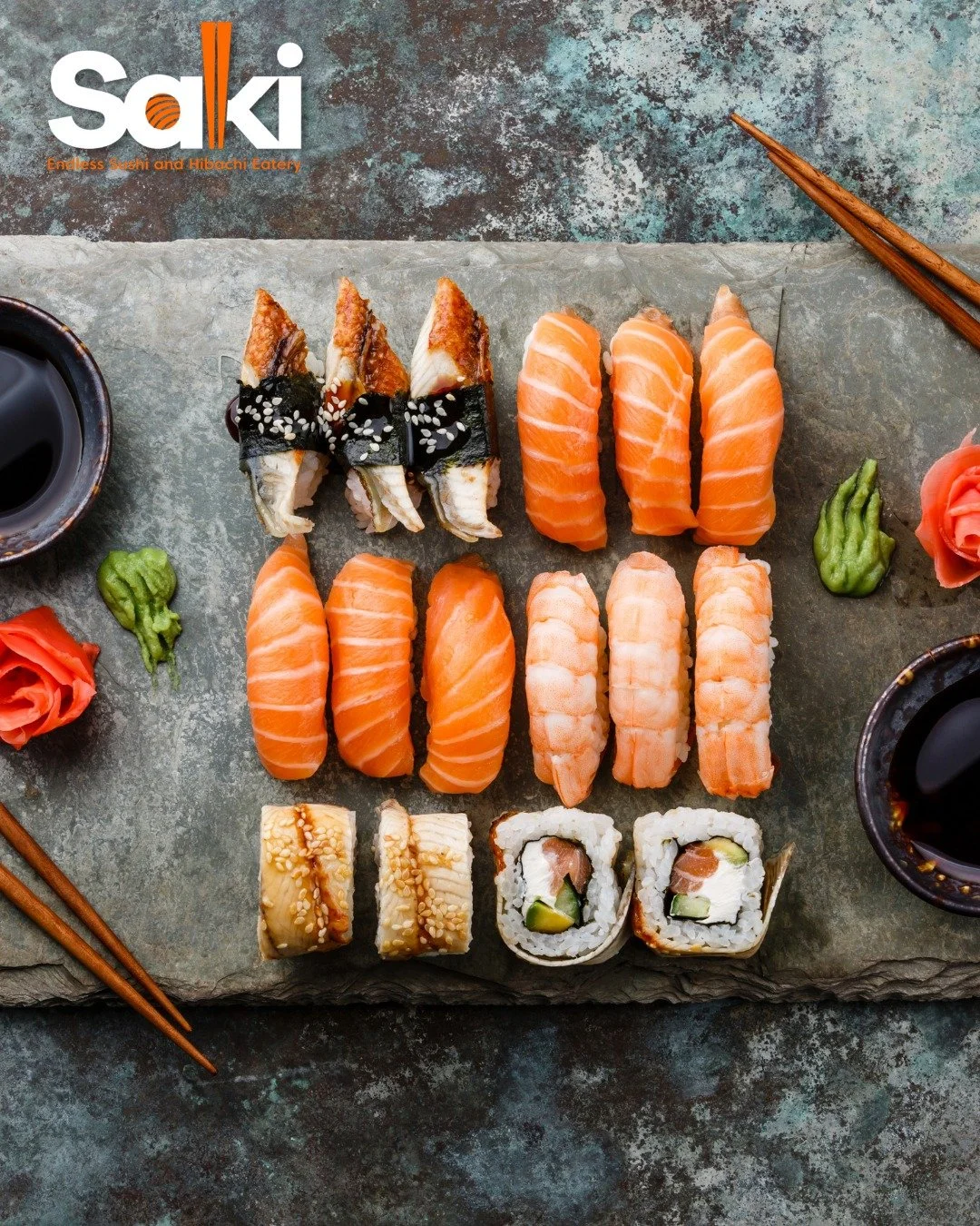 Assorted sushi platter with salmon, shrimp, and sushi rolls on a gray textured surface, accompanied by small dishes of soy sauce, pickled ginger, and wasabi, with chopsticks on the upper right and left sides.