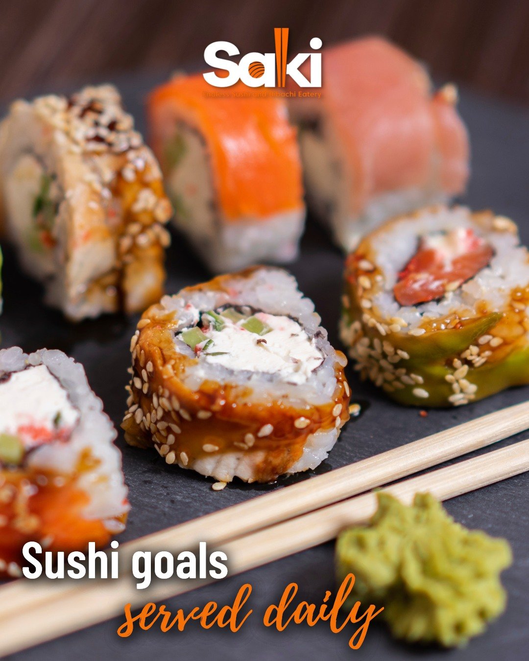 Close-up of assorted sushi rolls on a black slate platter with a small amount of wasabi and chopsticks.