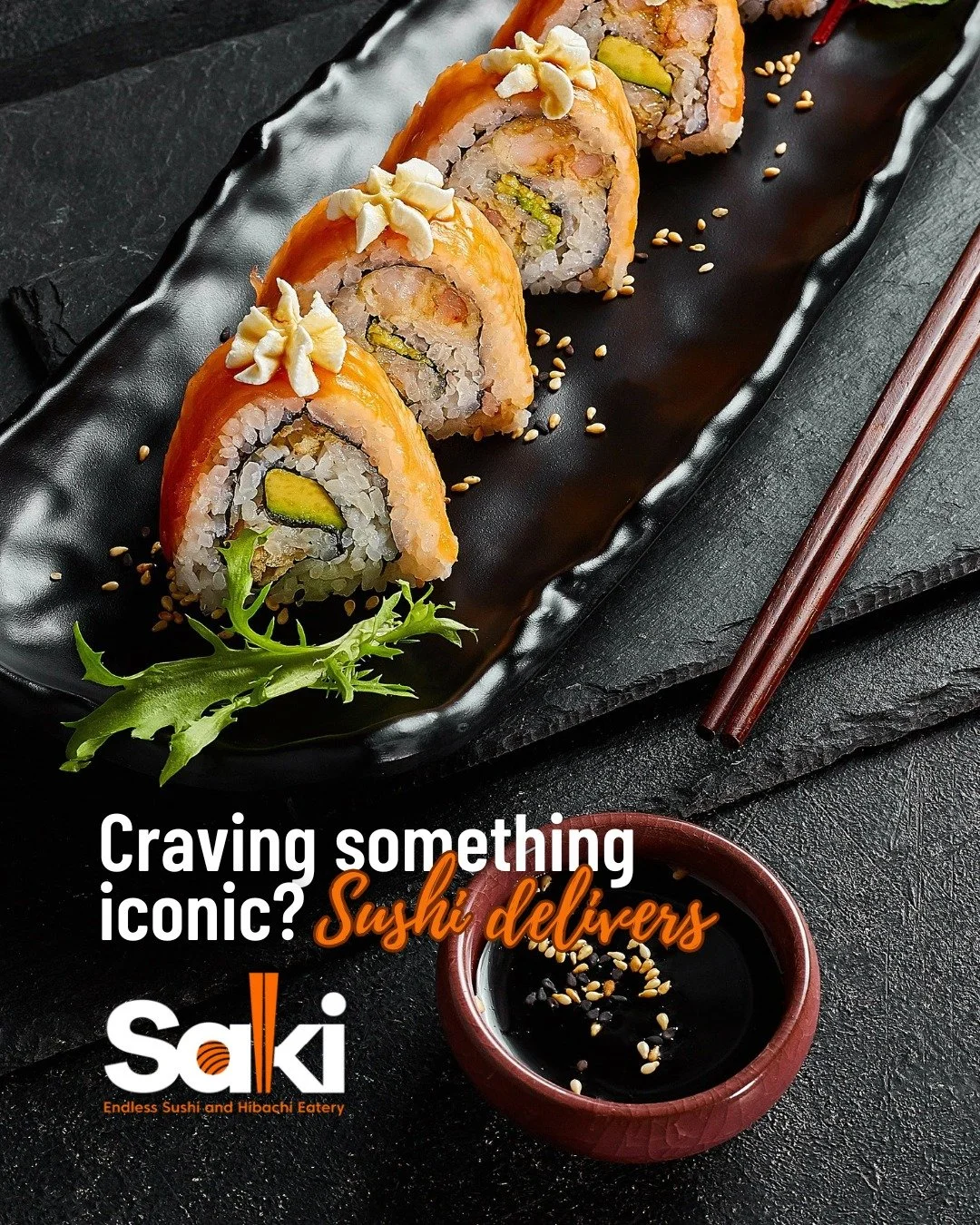 Sliced sushi rolls on a black plate with sesame seeds, garnished with some greens and a small bowl of soy sauce with sesame seeds, placed on a dark textured surface with chopsticks nearby.
