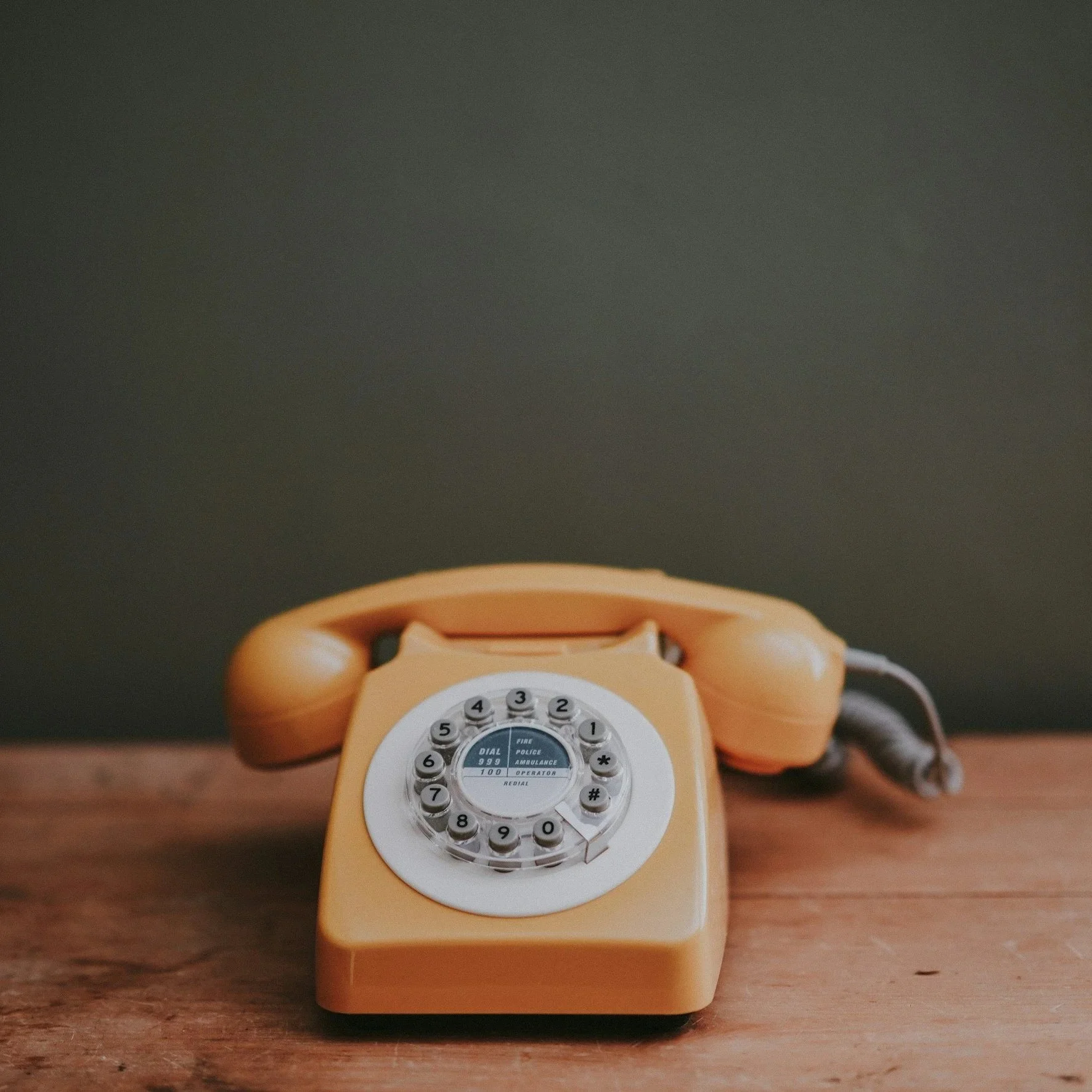 A vintage rotary telephone in yellow color with a dial pad on a wooden surface.