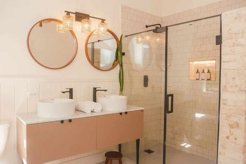 Modern bathroom with a double vanity, round mirrors, and a walk-in shower with beige tile walls and built-in shelves.