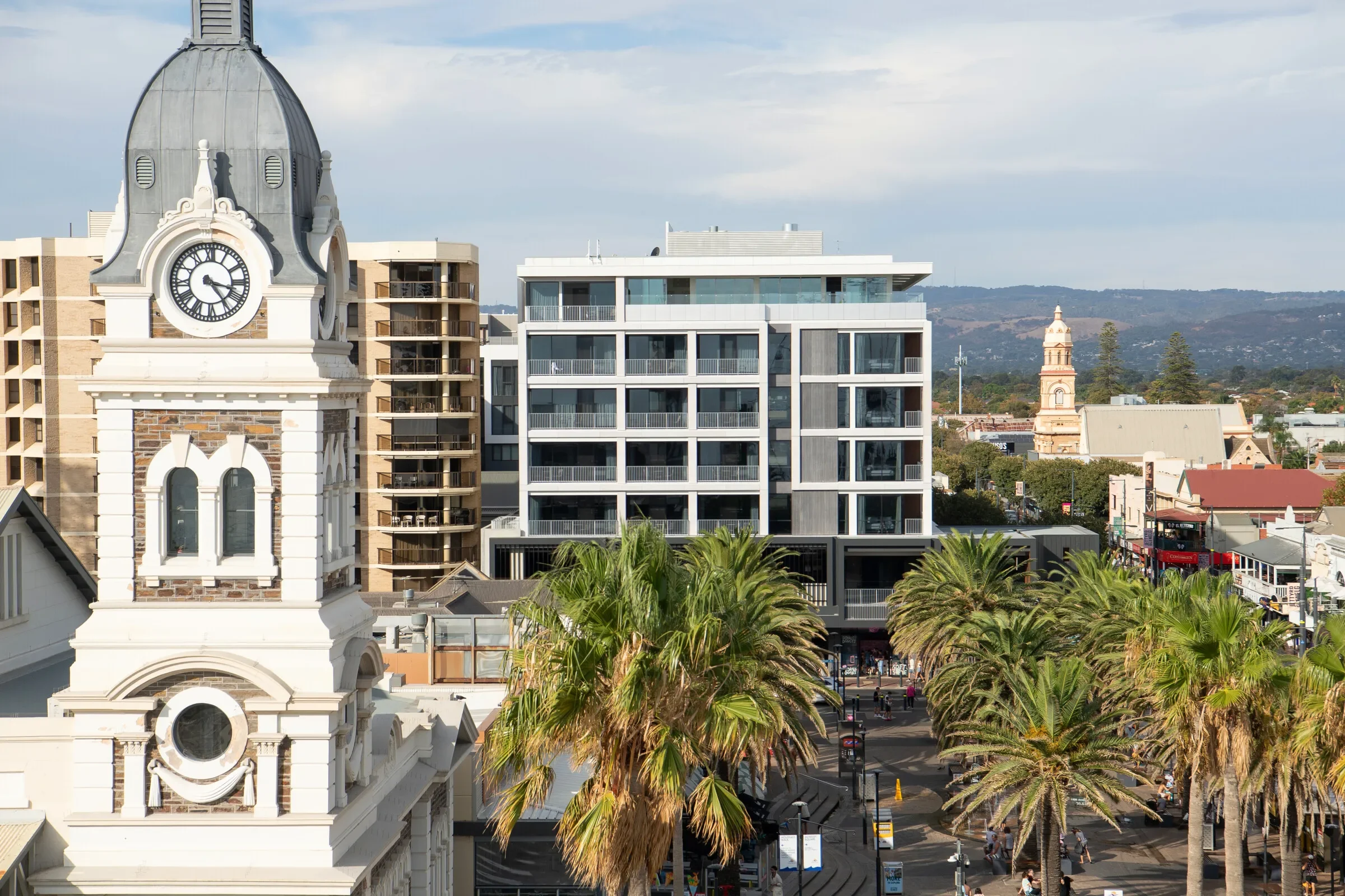 Cityscape featuring a historic clock tower, modern buildings, and palm trees