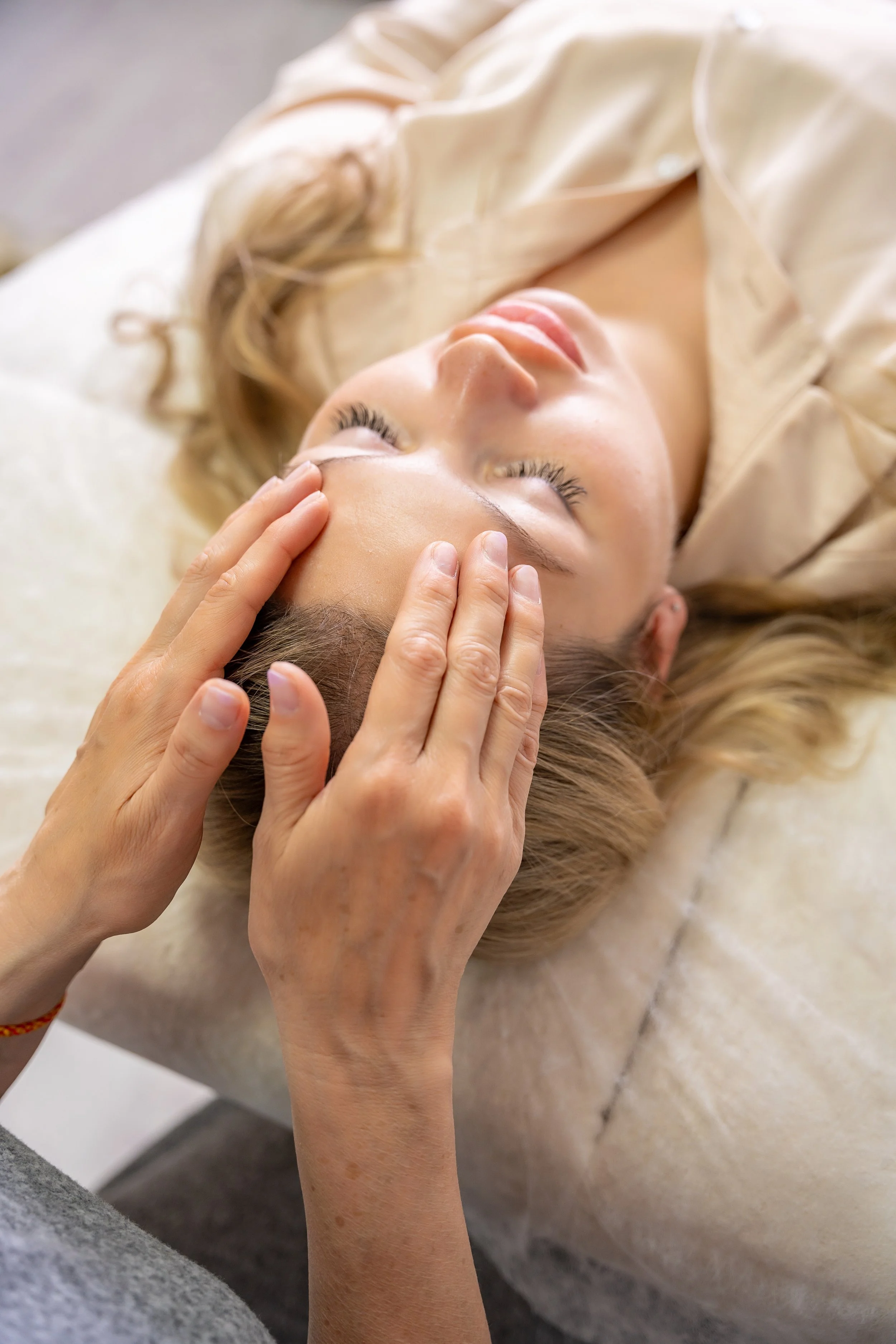 Person receiving energy healing, lying down on a surface with a beige or cream-colored blanket or cloth around them.