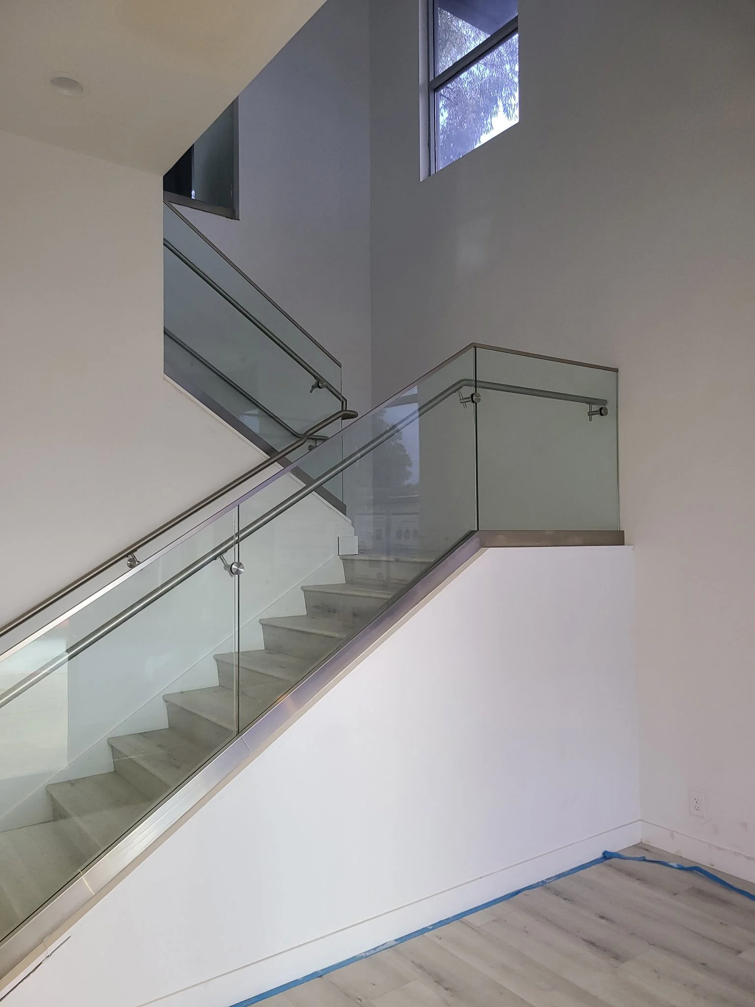 Empty staircase with glass railing and metal handrail inside a modern home.